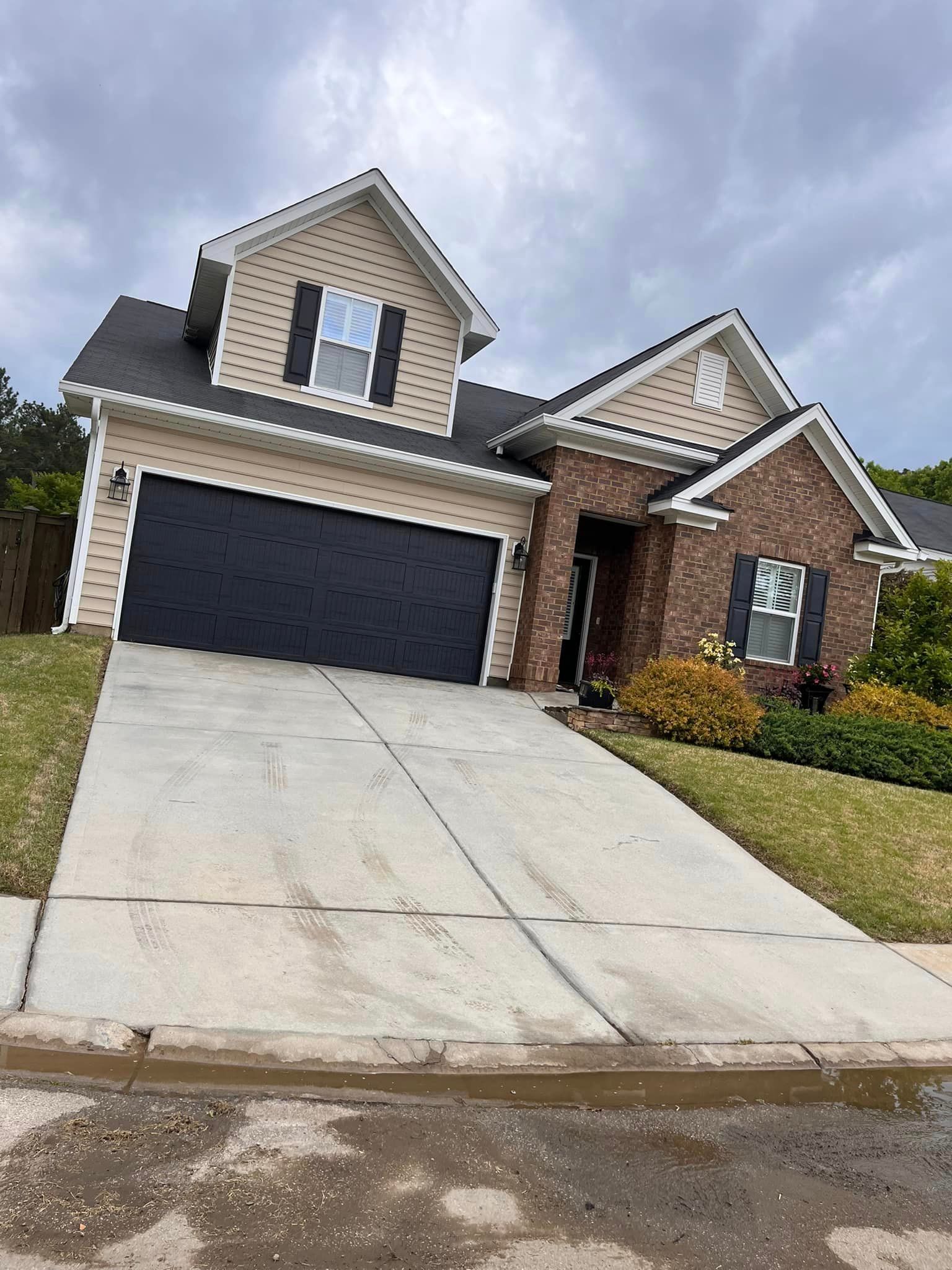 A brick house with a black garage door and a concrete driveway.