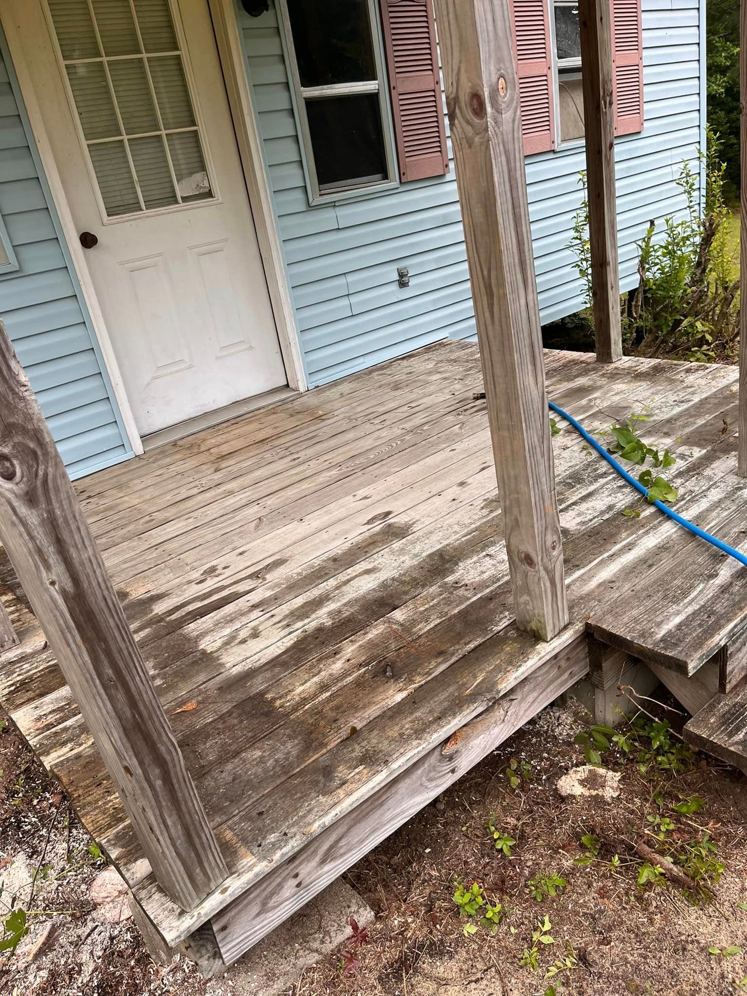 A wooden porch with a hose attached to it in front of a blue house.