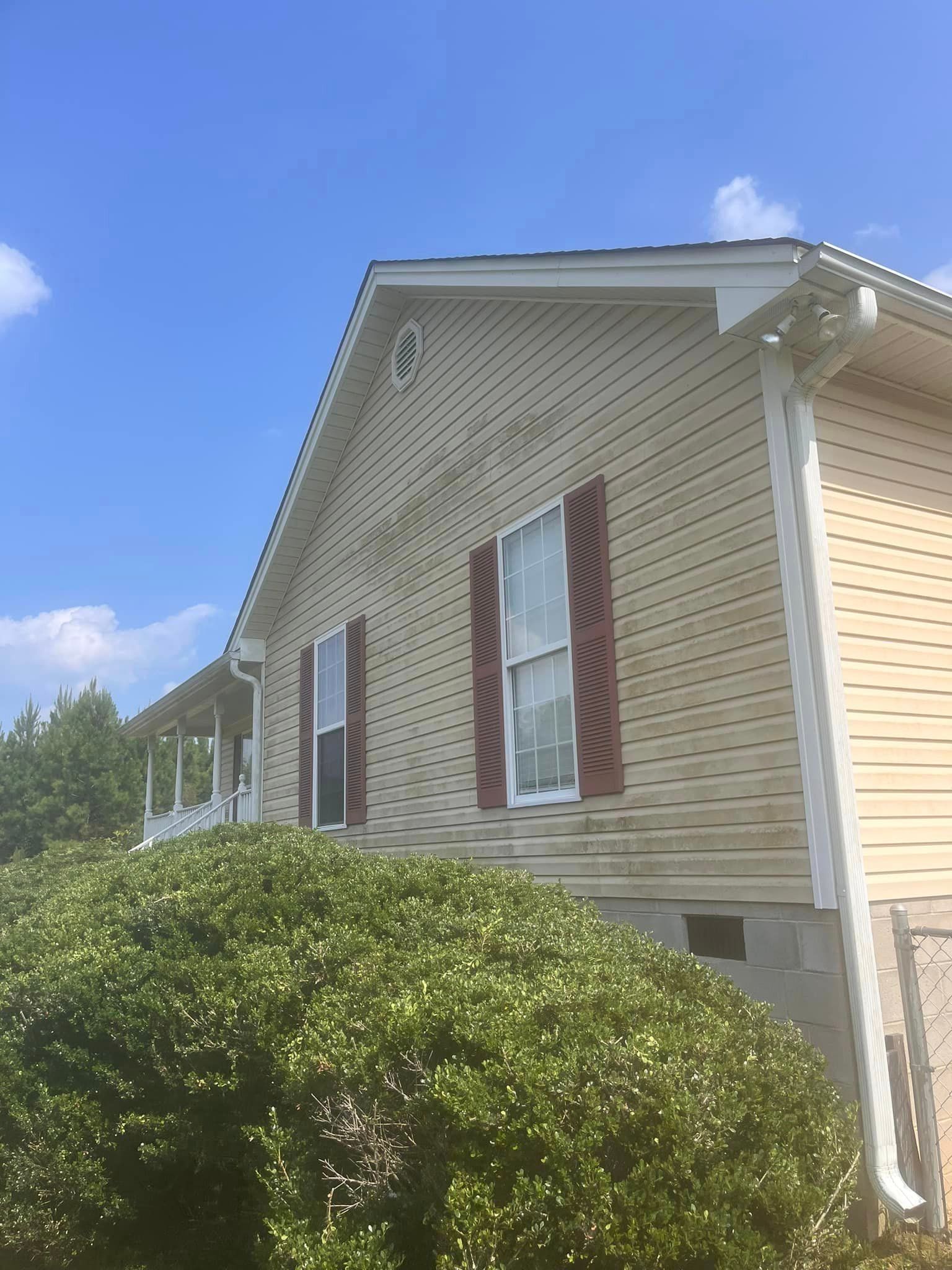 A house with a lot of bushes in front of it and a blue sky in the background.
