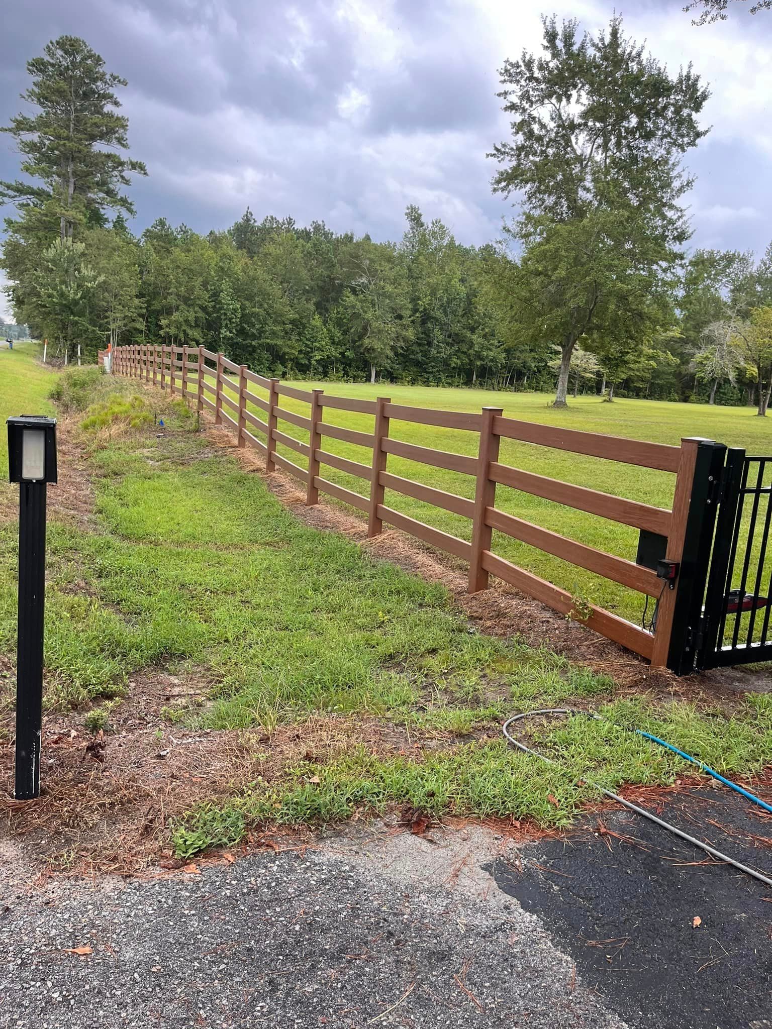 A wooden fence surrounds a grassy field with trees in the background.