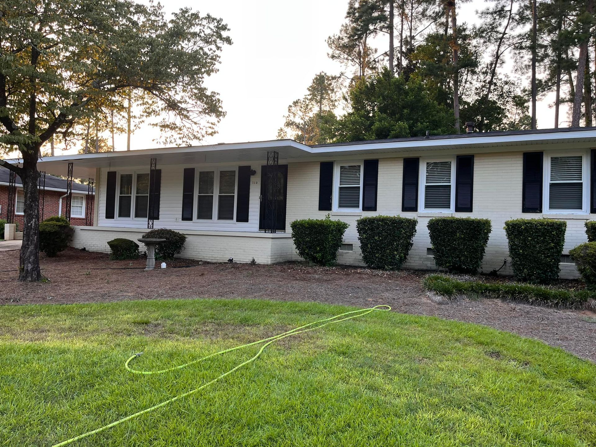 A white house with black shutters and bushes in front of it