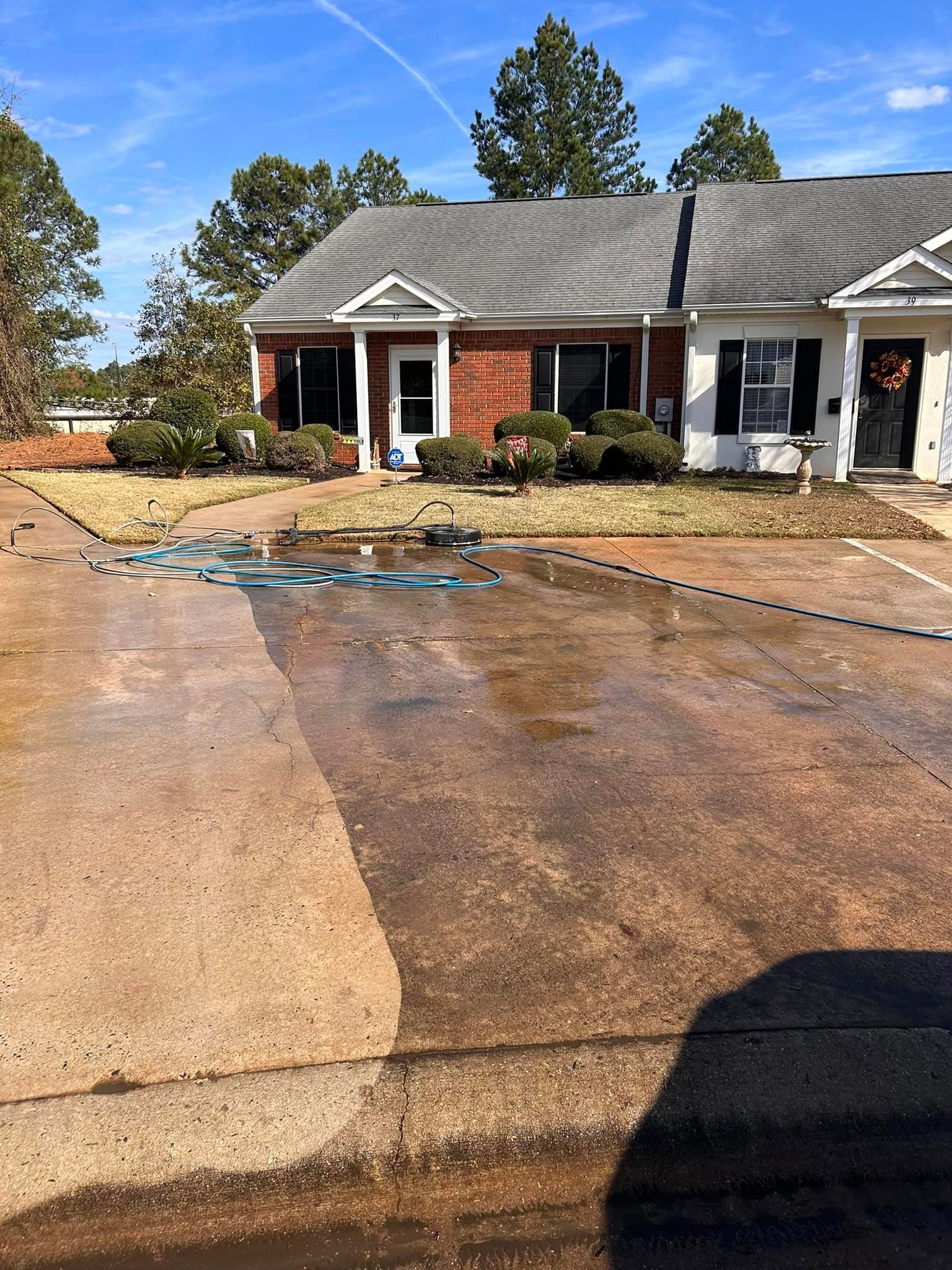 A brick house with a driveway that is being cleaned with a hose.