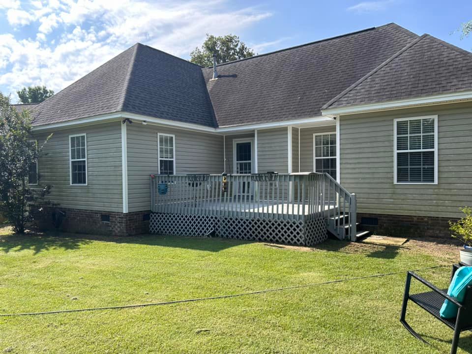 The back of a house with a large deck and a bench in front of it.