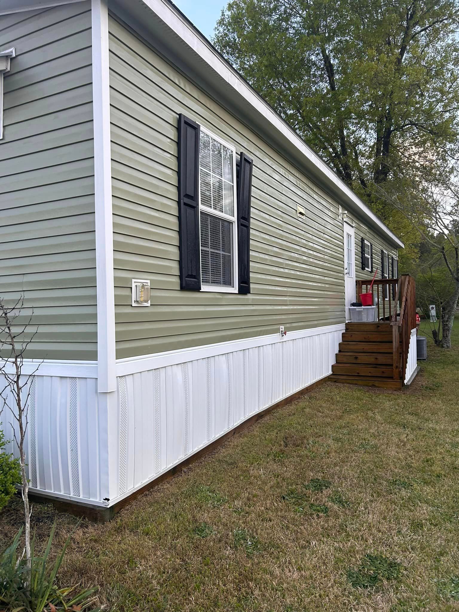 A mobile home with a green siding and white trim is sitting on top of a lush green field.