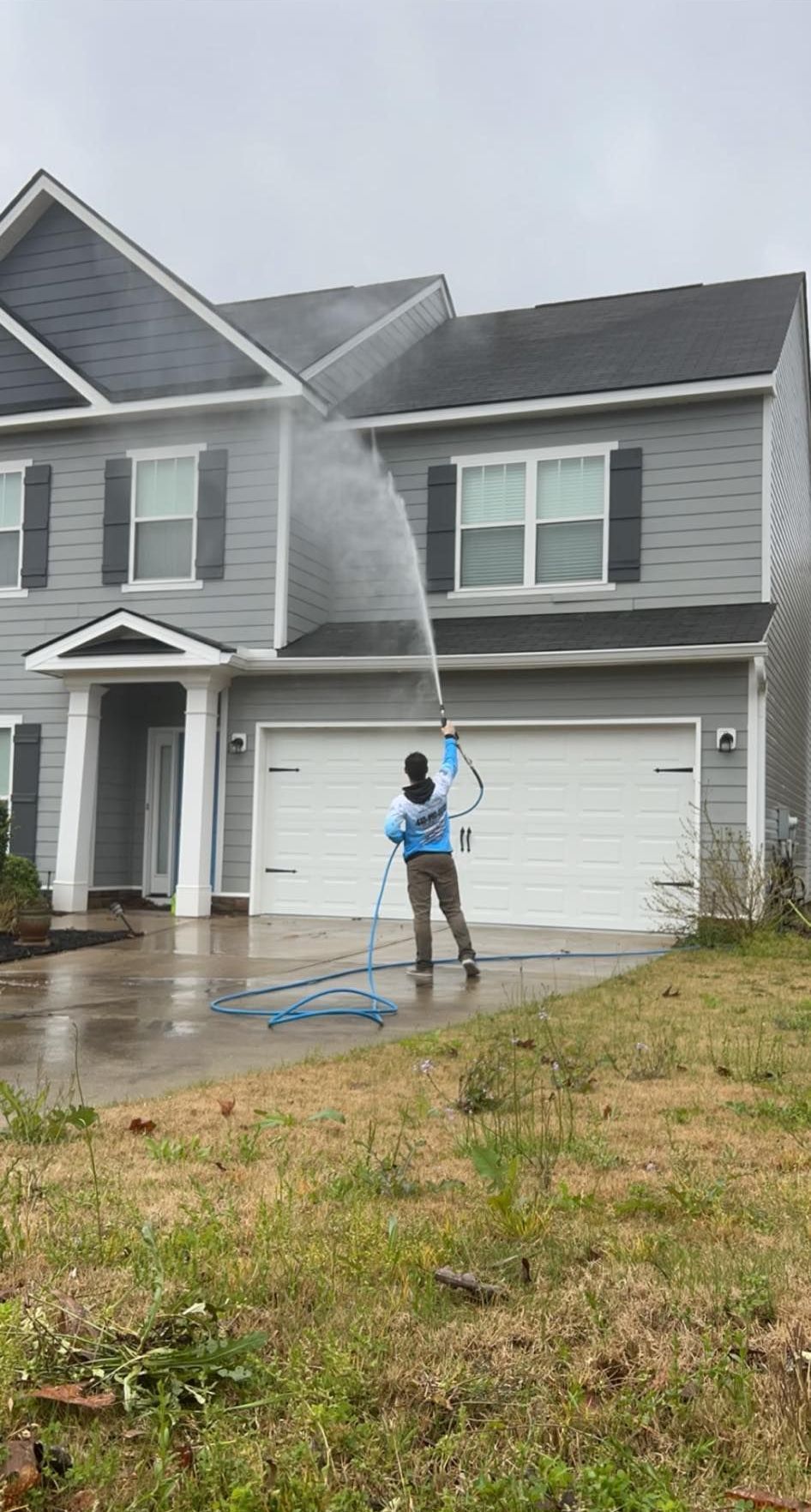 A man is cleaning the roof of a house with a pressure washer.
