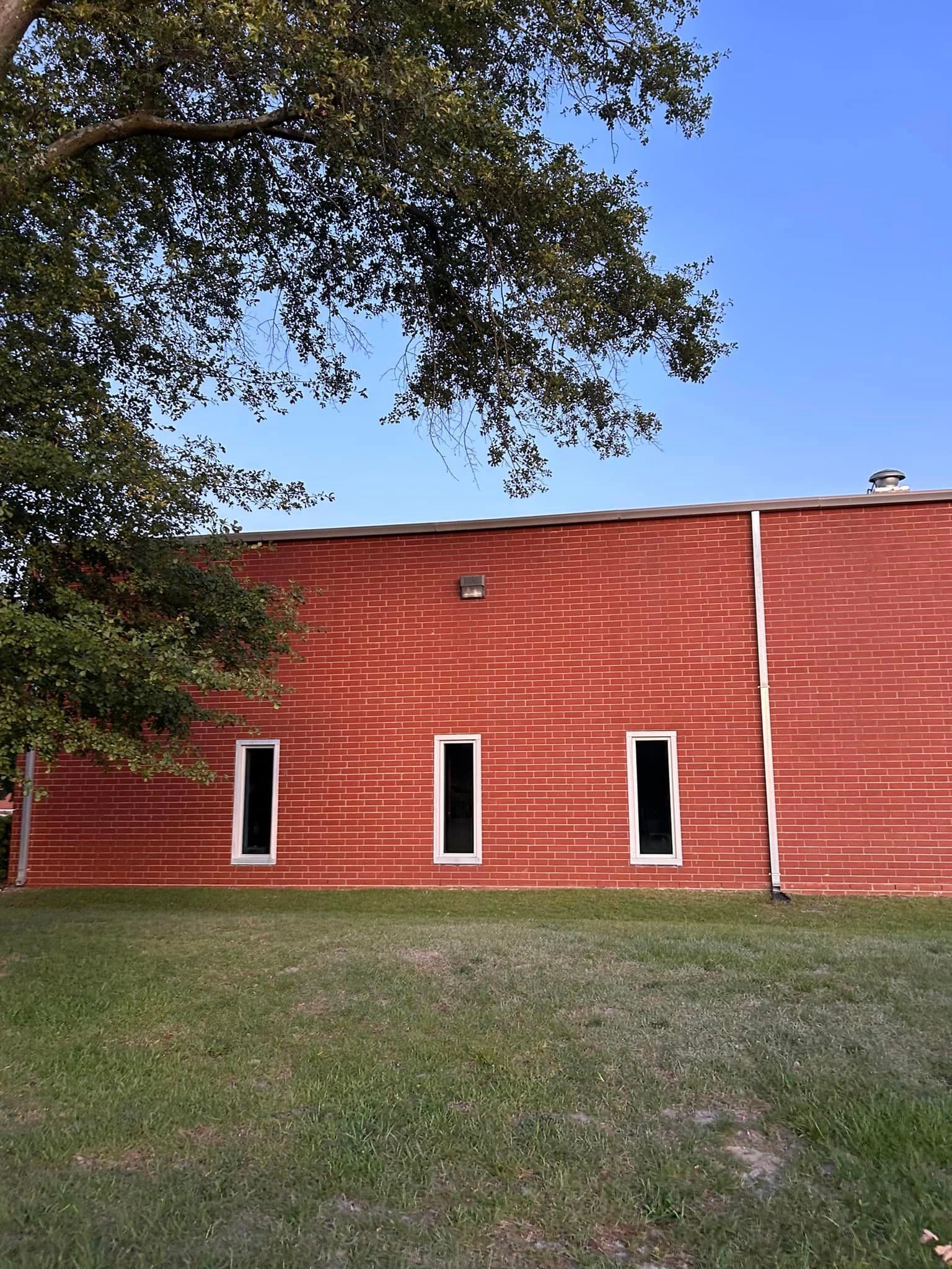 A red building with three windows and a tree in front of it