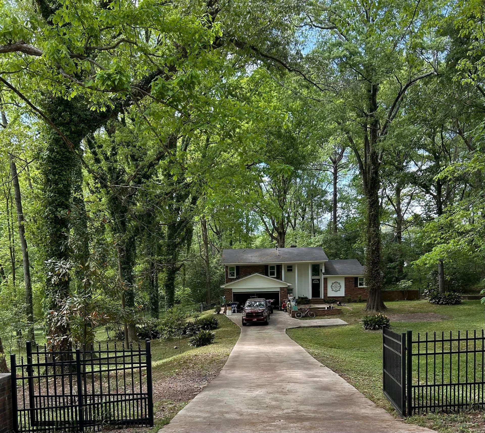 A car is parked in the driveway of a house surrounded by trees.