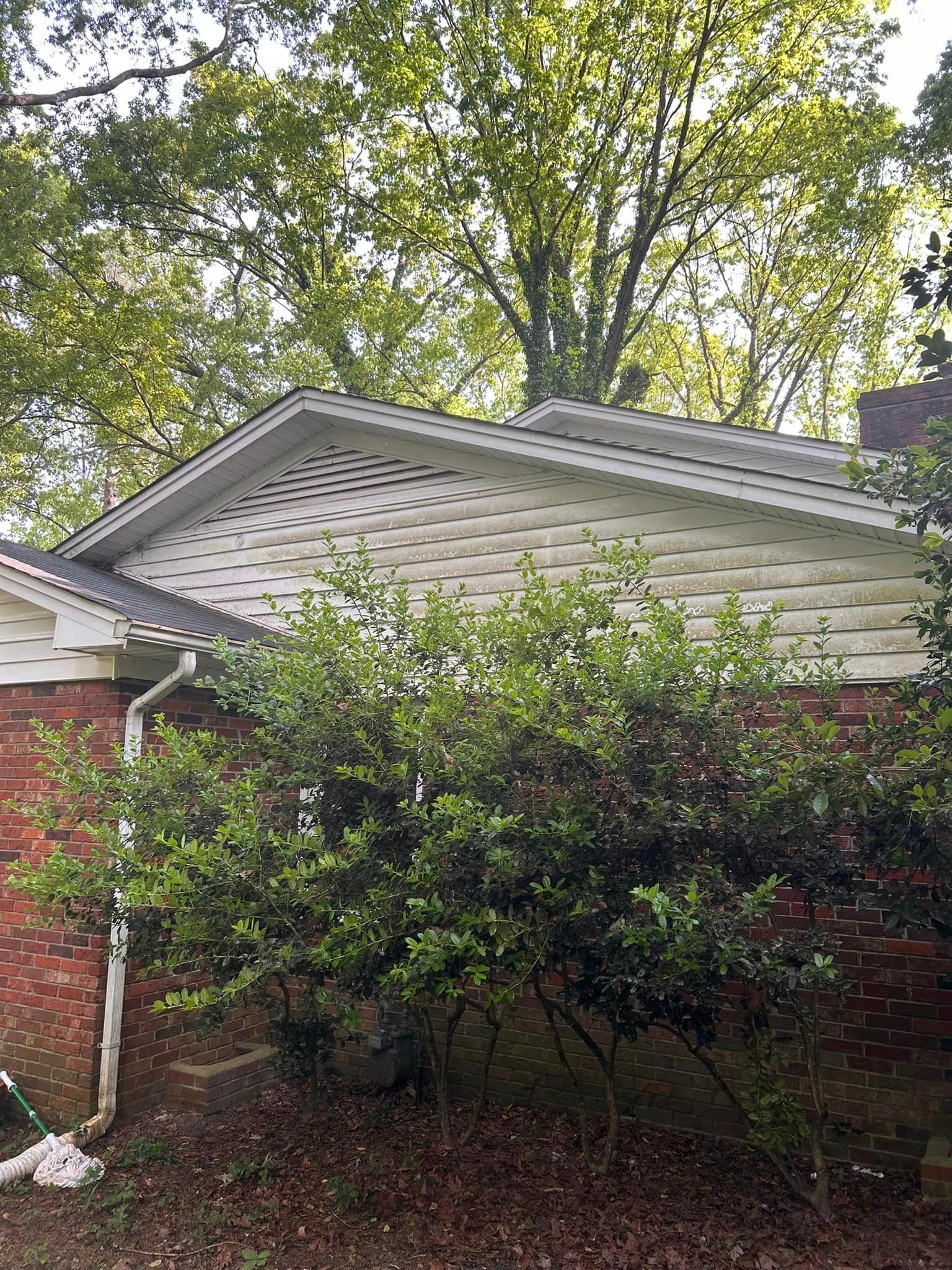 A brick house with a white siding and a tree in front of it.