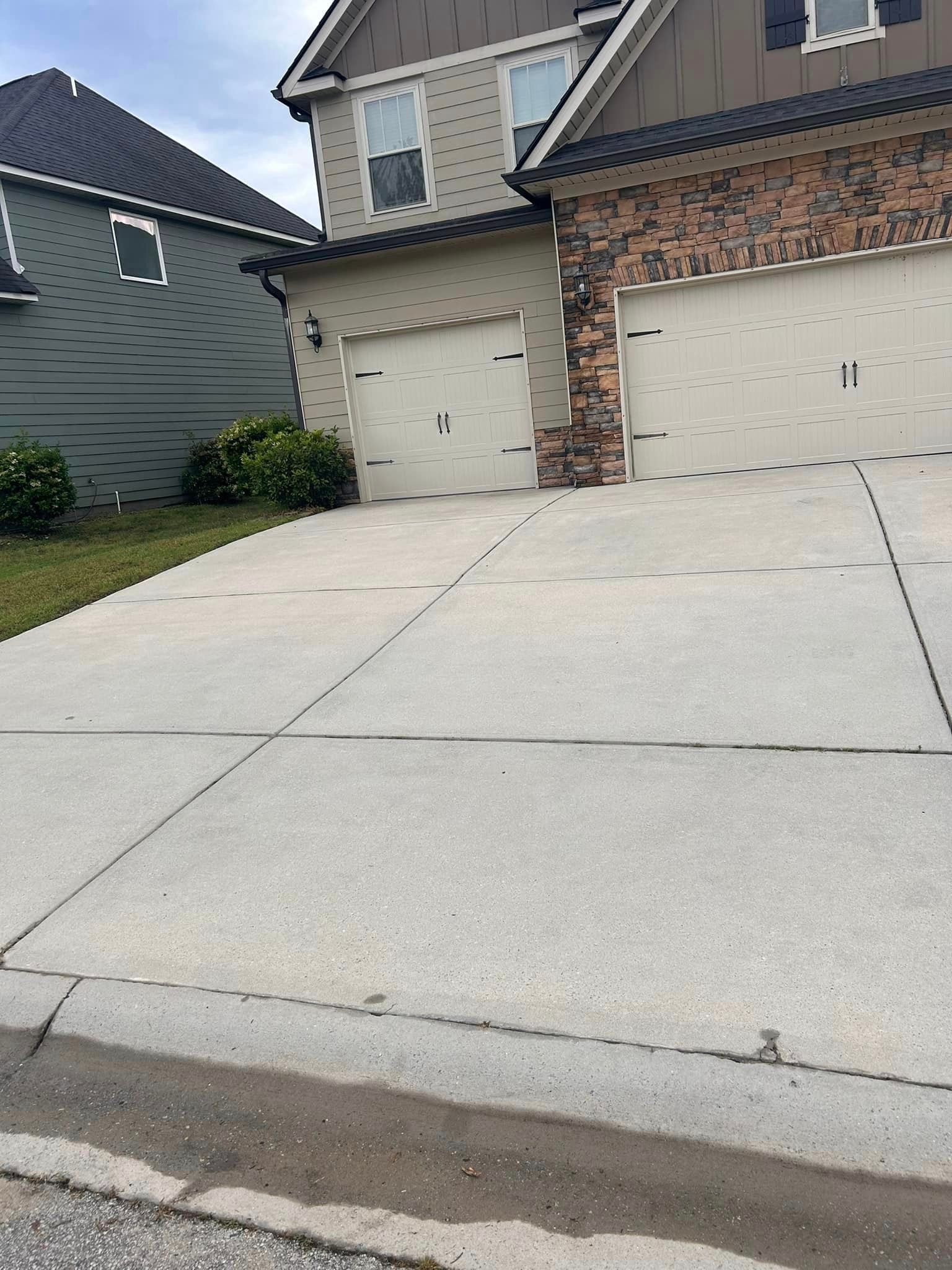 A concrete driveway in front of a house with two garage doors.