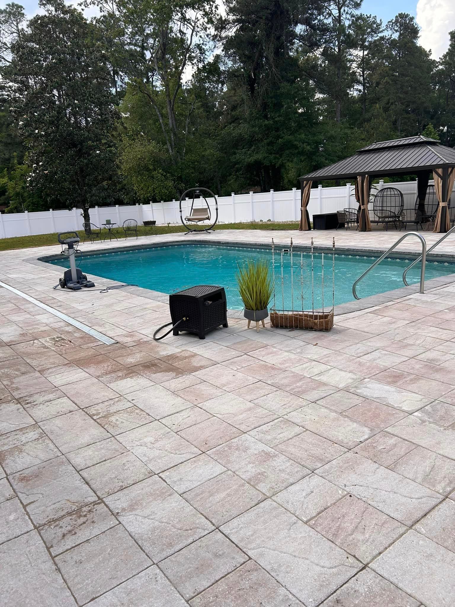A large swimming pool is surrounded by a tiled patio and a gazebo.