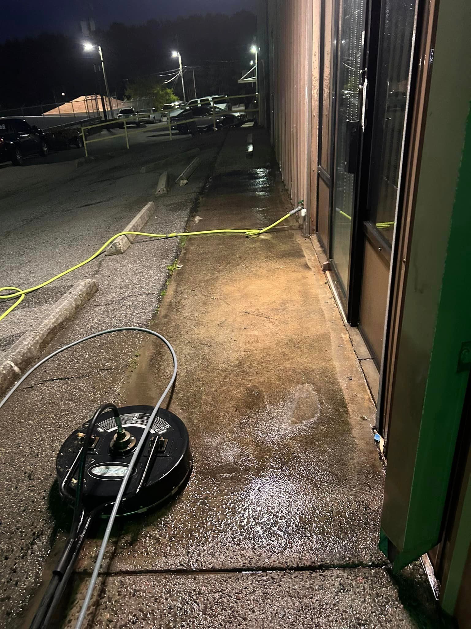 A pressure washer is being used to clean a sidewalk outside of a building.