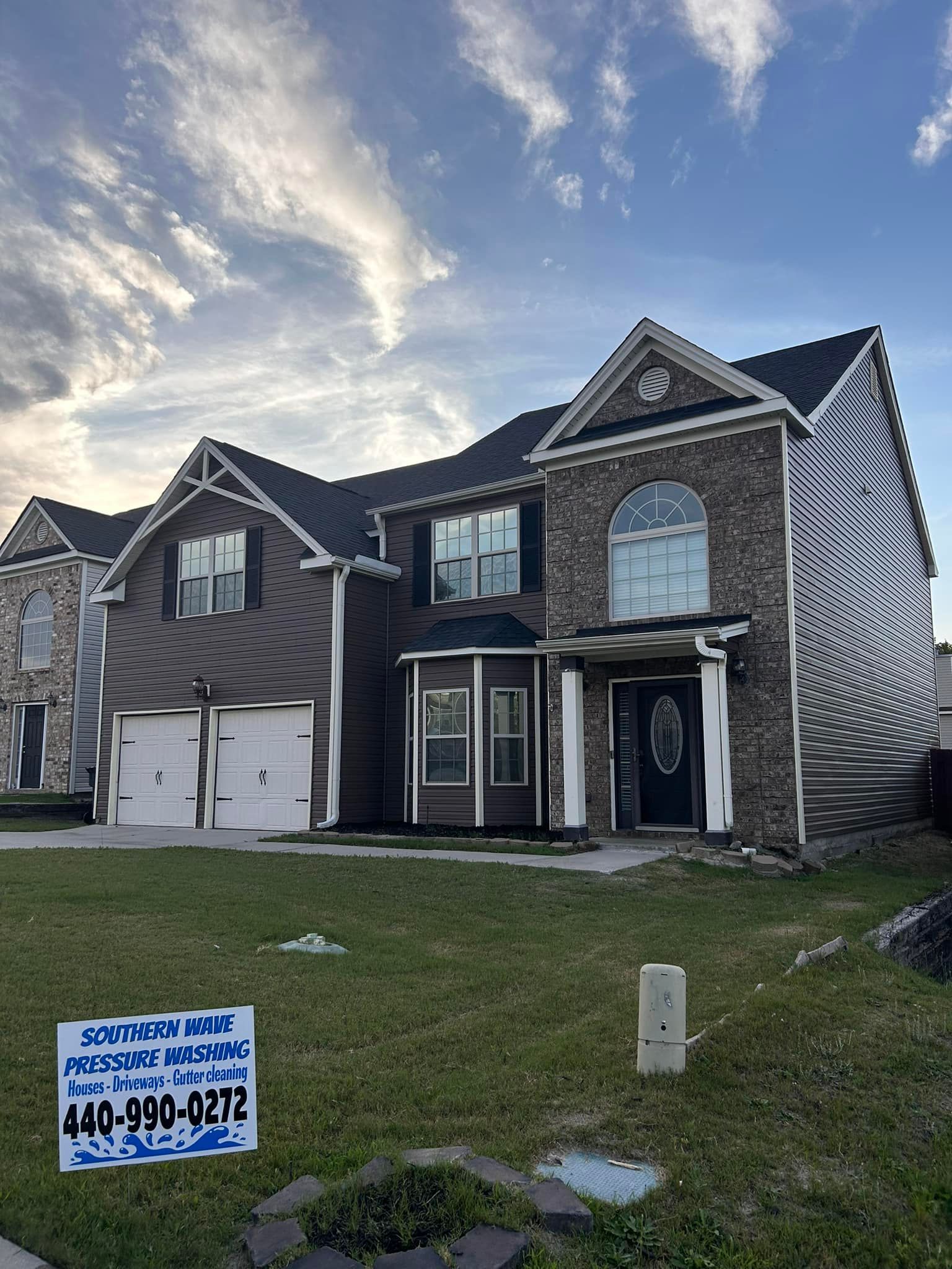 A large brick house with a black roof and a sign in front of it.