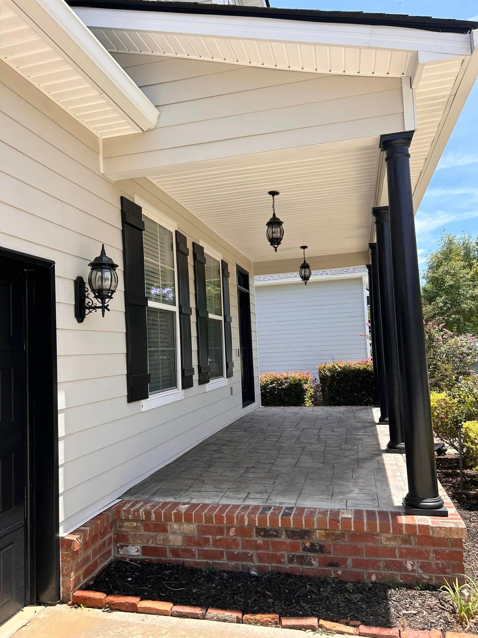The front porch of a white house with black shutters and a black door.