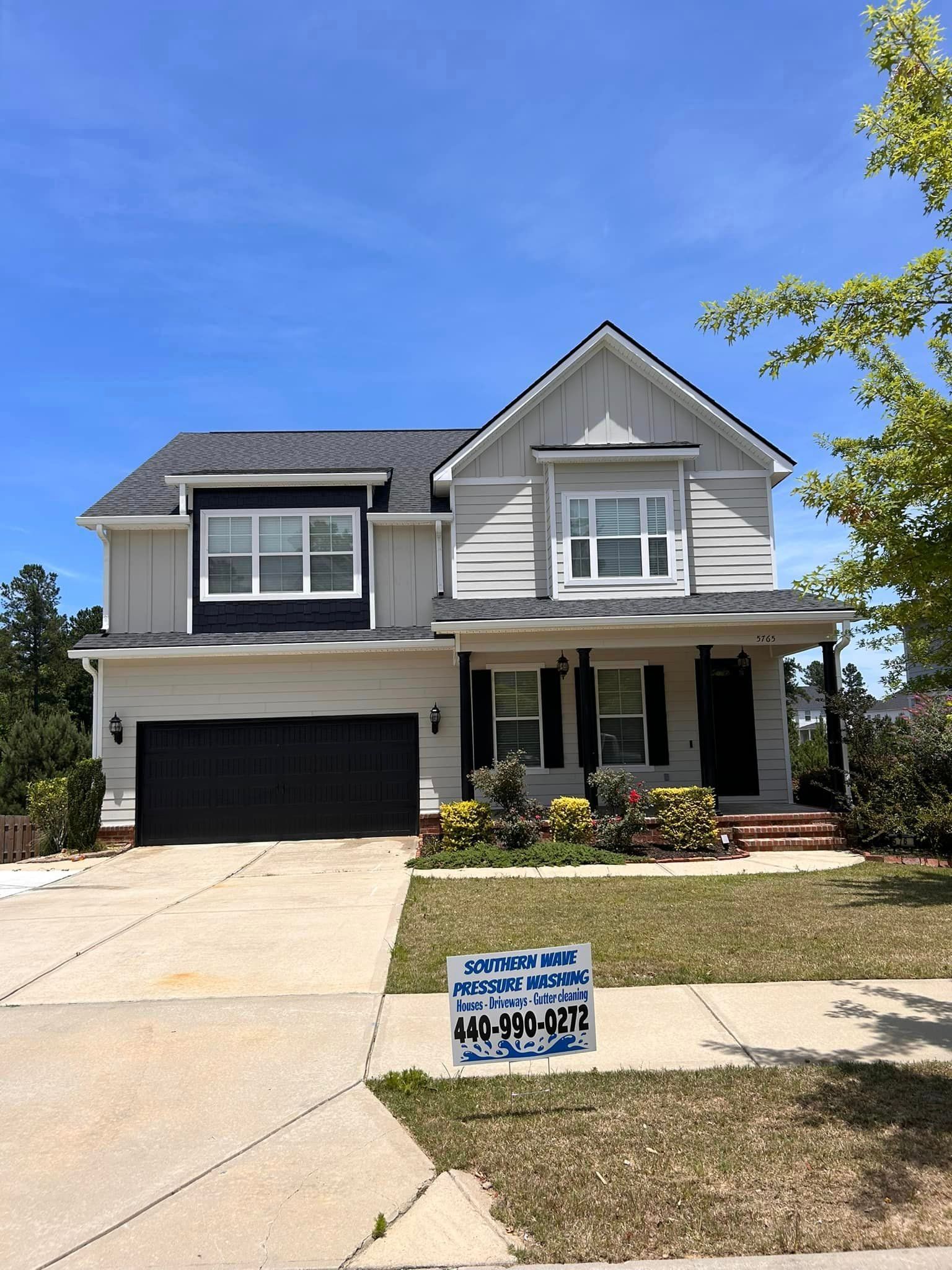 A large white house with a black garage door and a sign in front of it.