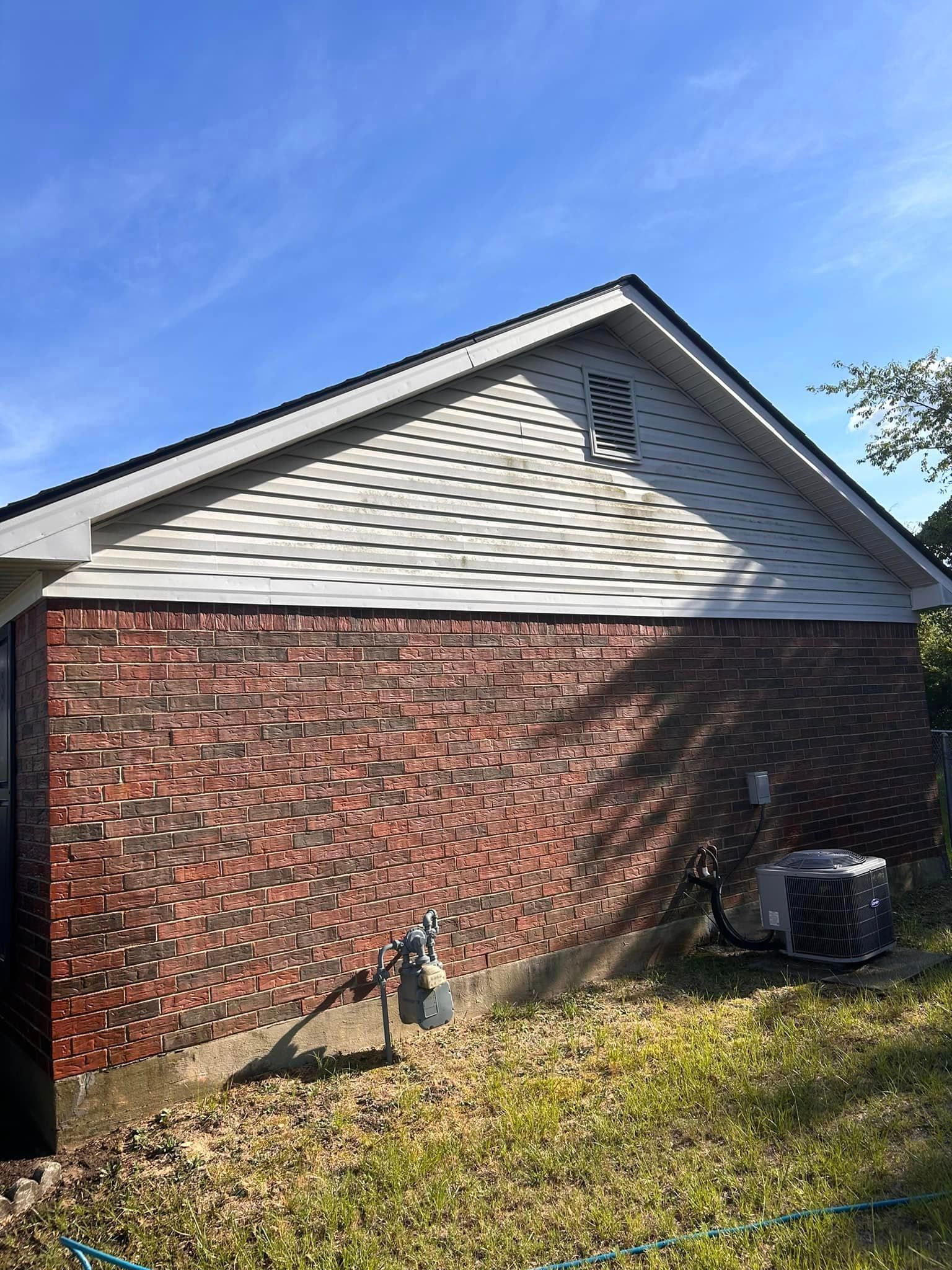 A brick house with a white siding and an air conditioner in the backyard.