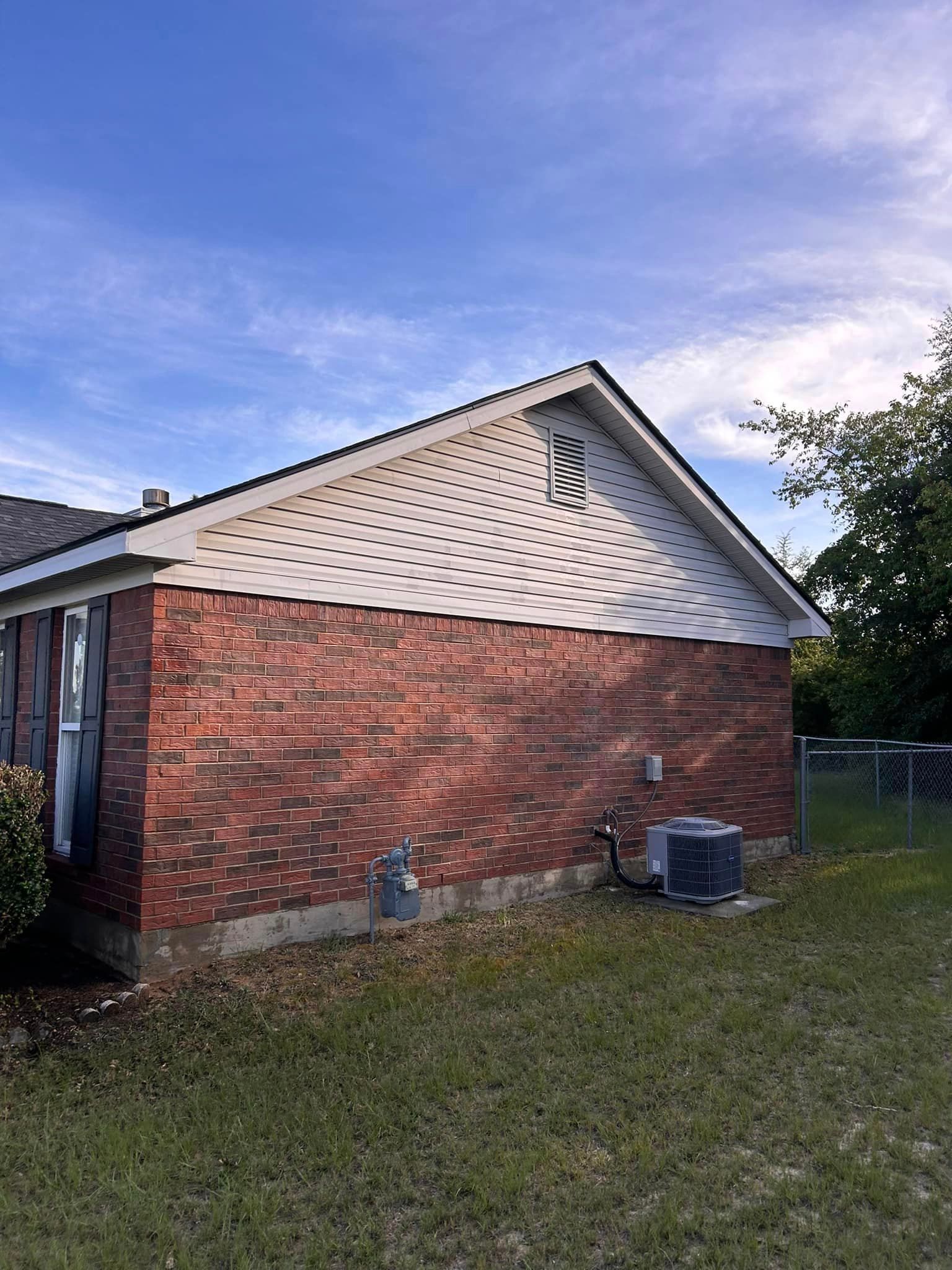 A brick house with a white siding and an air conditioner in the backyard.