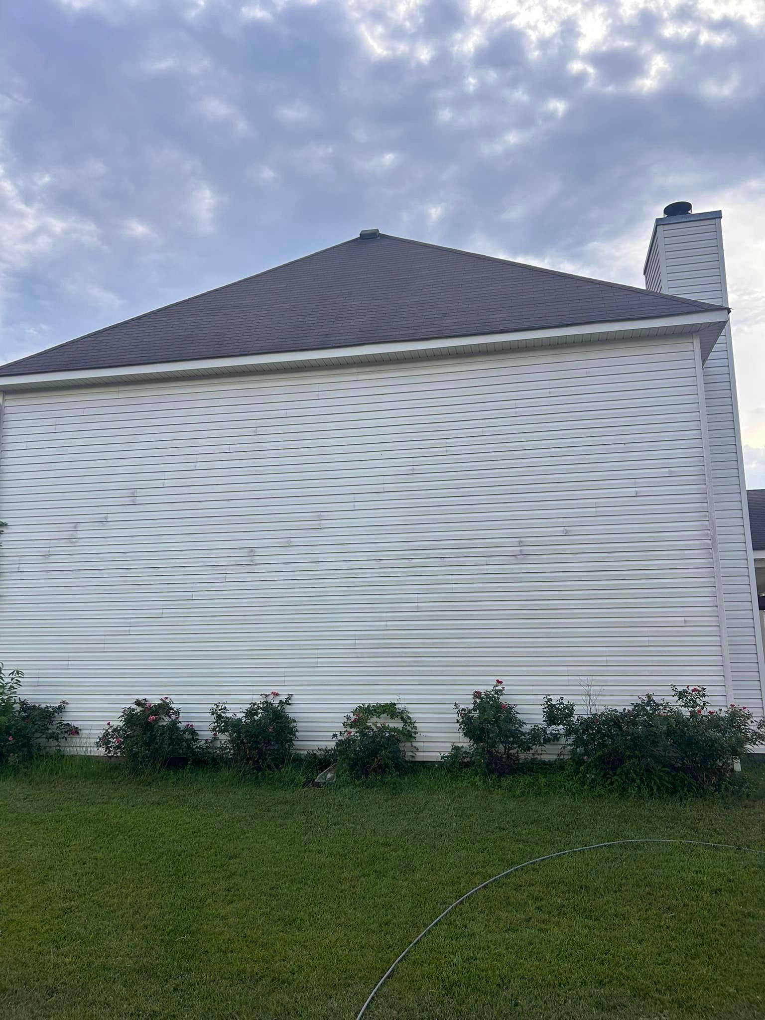 A white house with a black roof is sitting on top of a lush green field.