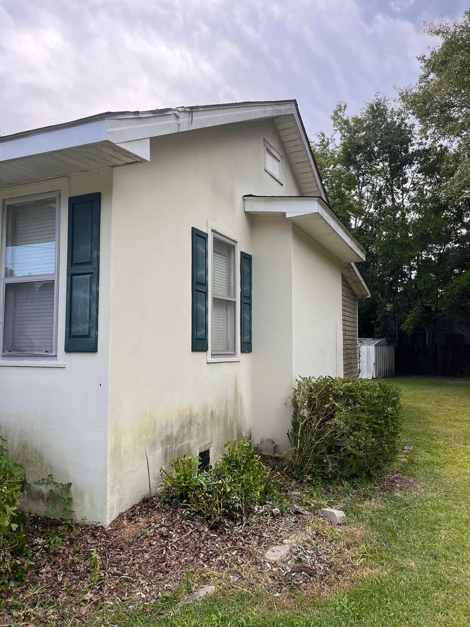 A white house with blue shutters is sitting on top of a lush green field.