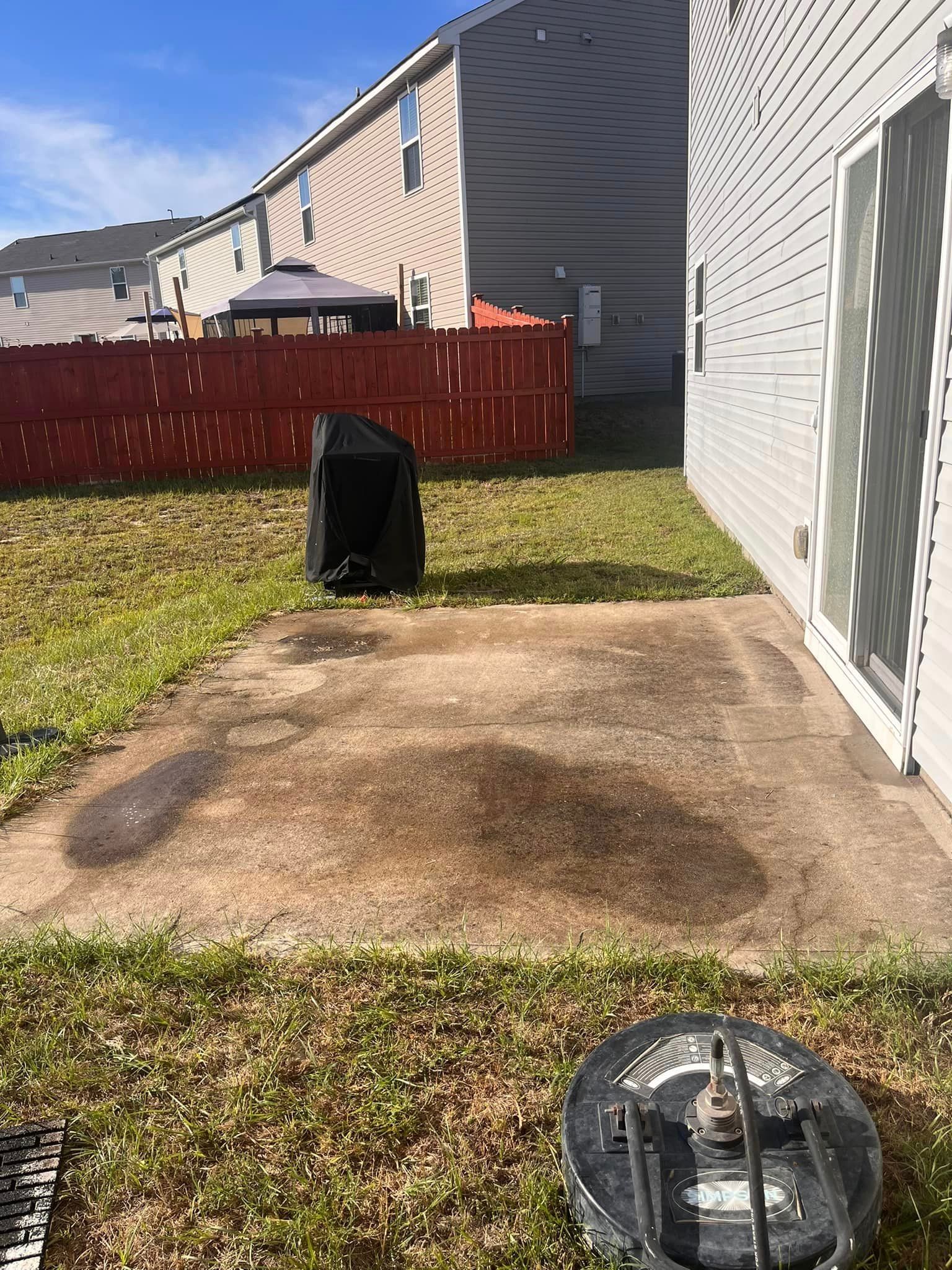 A backyard with a concrete patio and a red fence.