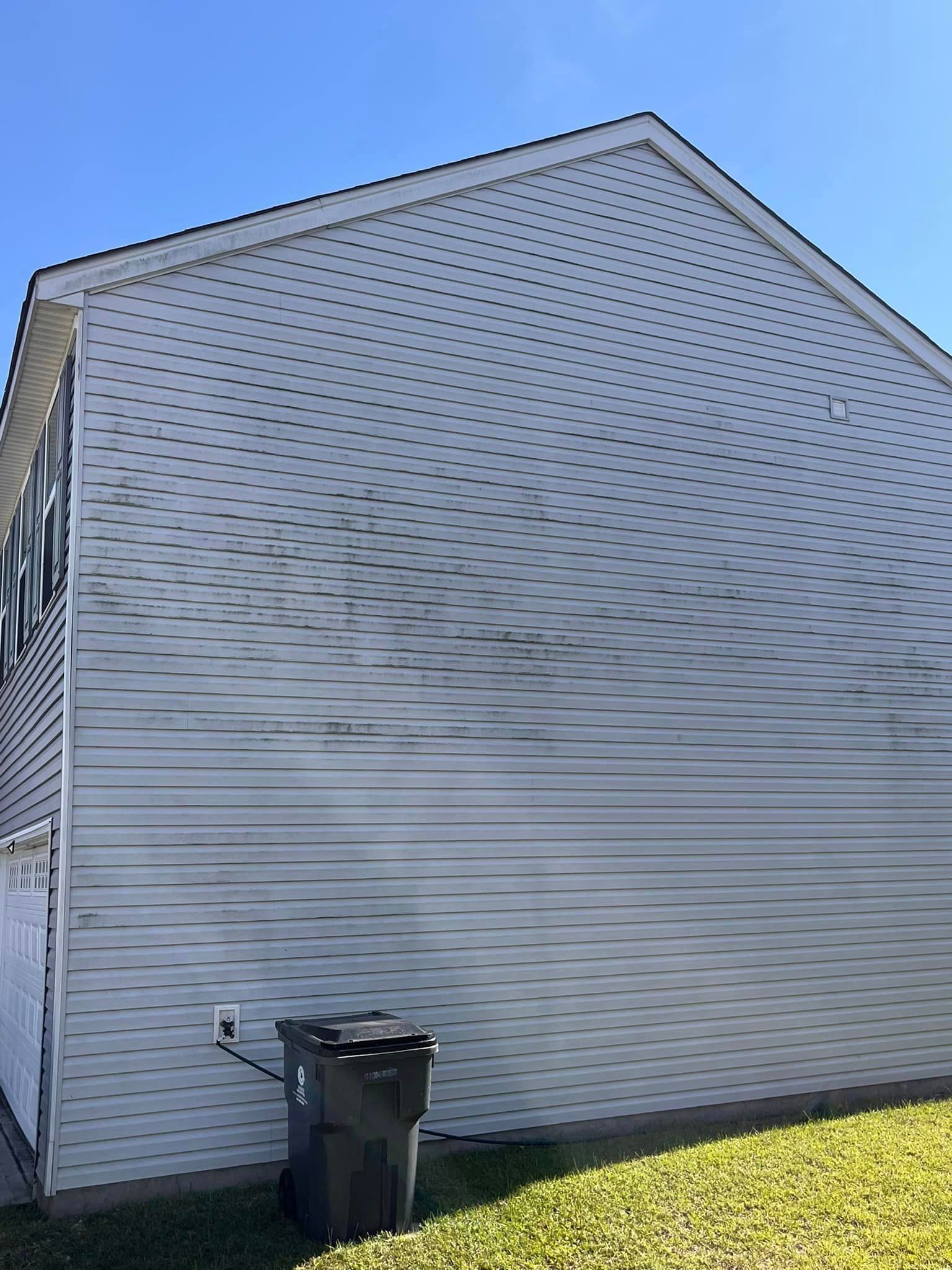 A white house with a trash can on the side of it.