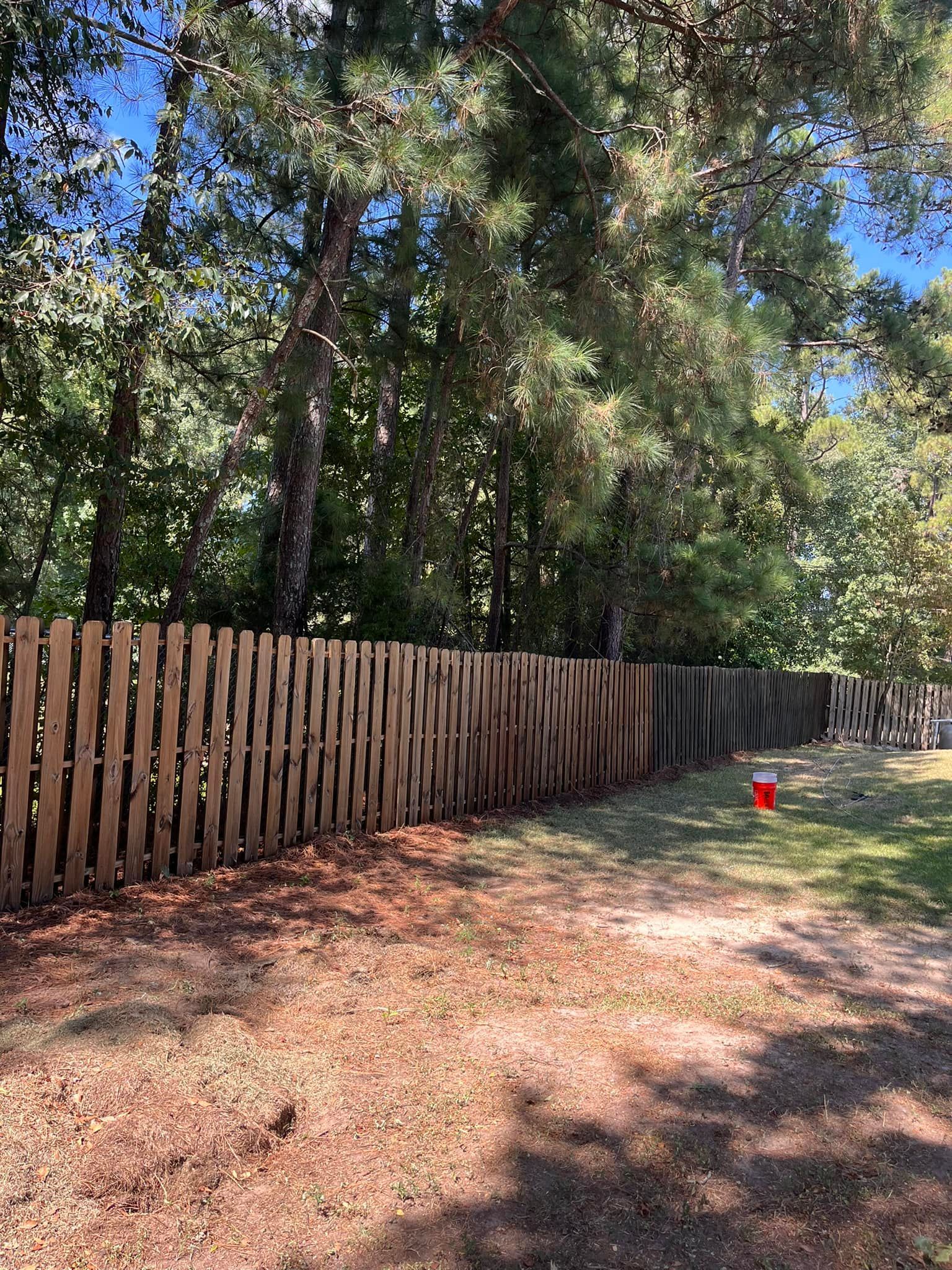 A wooden fence is surrounded by trees on a dirt road.