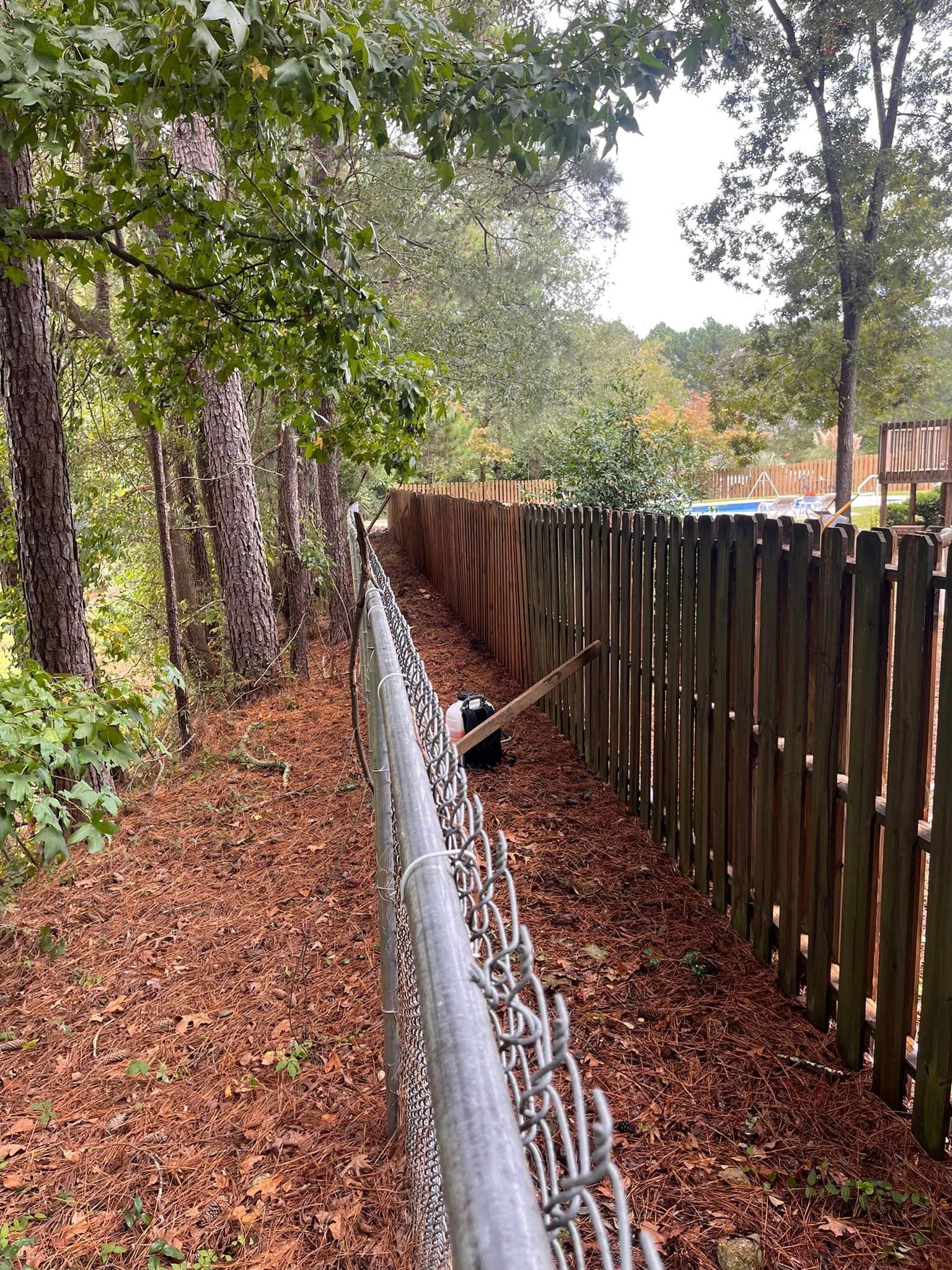 A chain link fence is surrounded by trees and dirt.