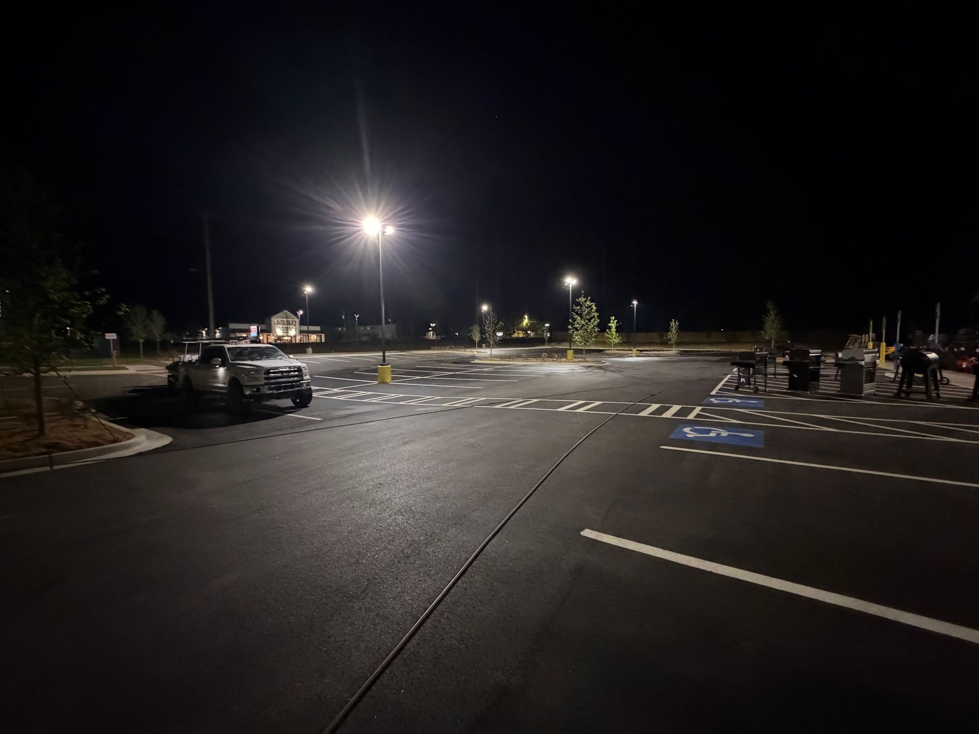 Nighttime parking lot with streetlights, a few cars, and painted parking spaces.