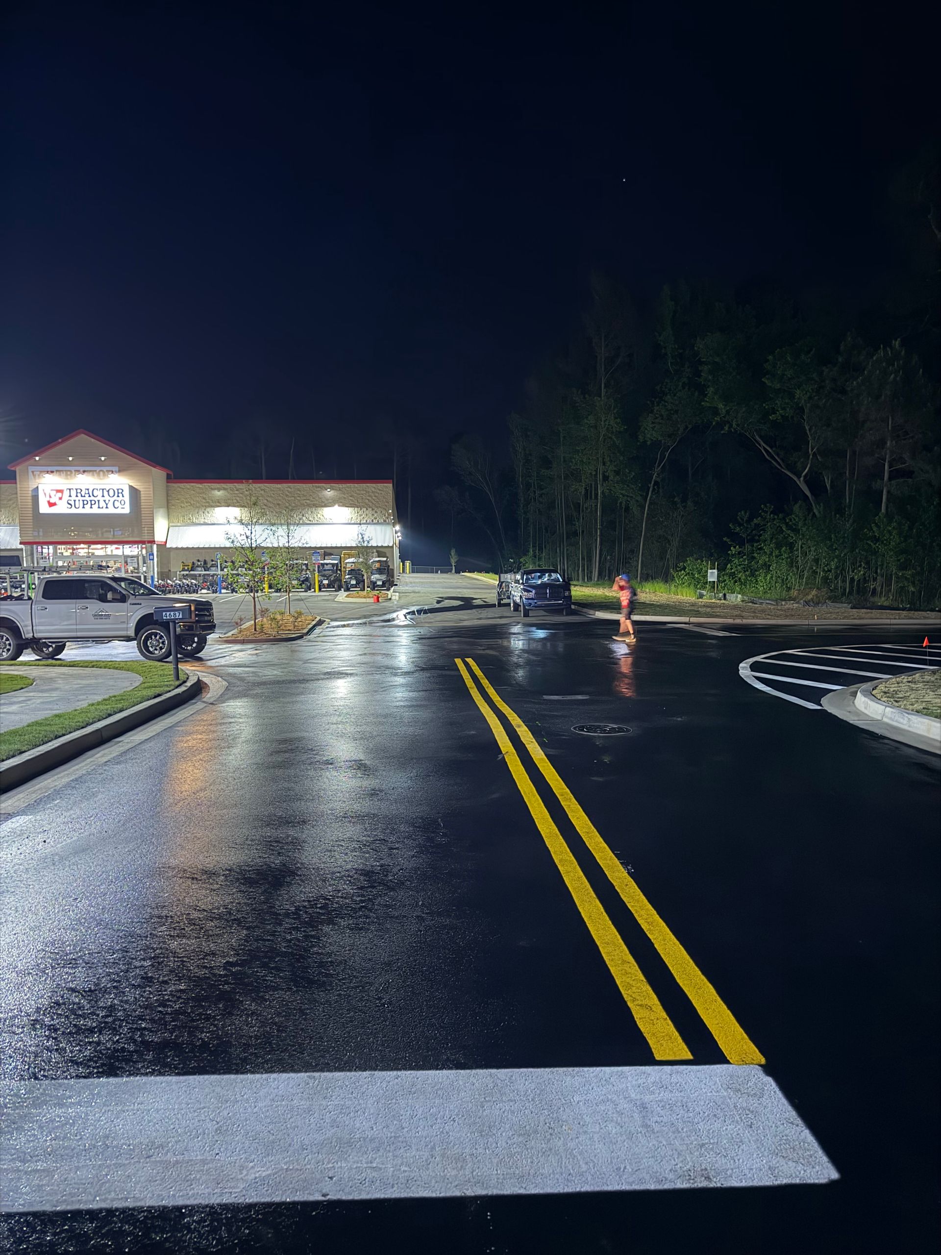 Rainy parking lot at night with wet pavement, double yellow lines, and a lit store in the distance