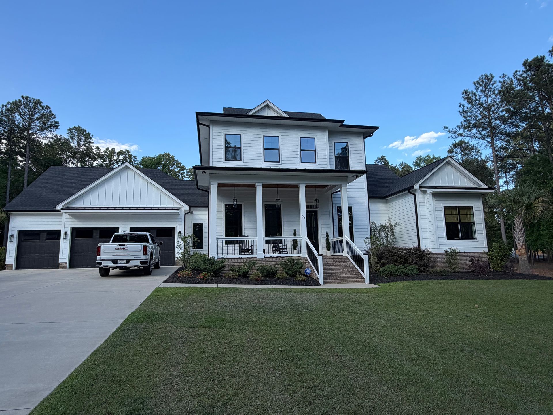 Large two-story white house with a front porch, attached garage, and wide driveway under a clear blue sky