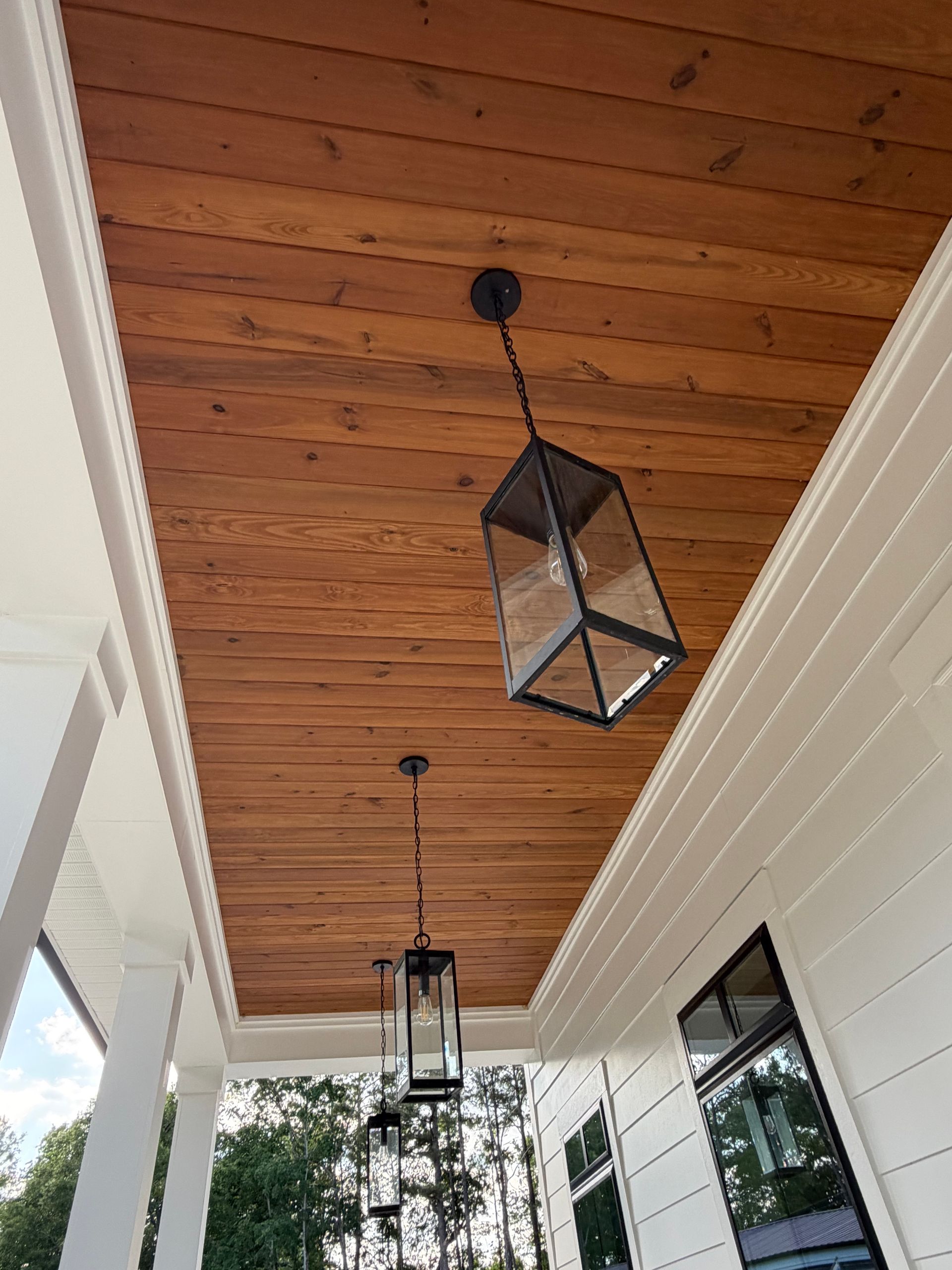Covered porch ceiling with wooden planks and black hanging lanterns beside white siding and windows