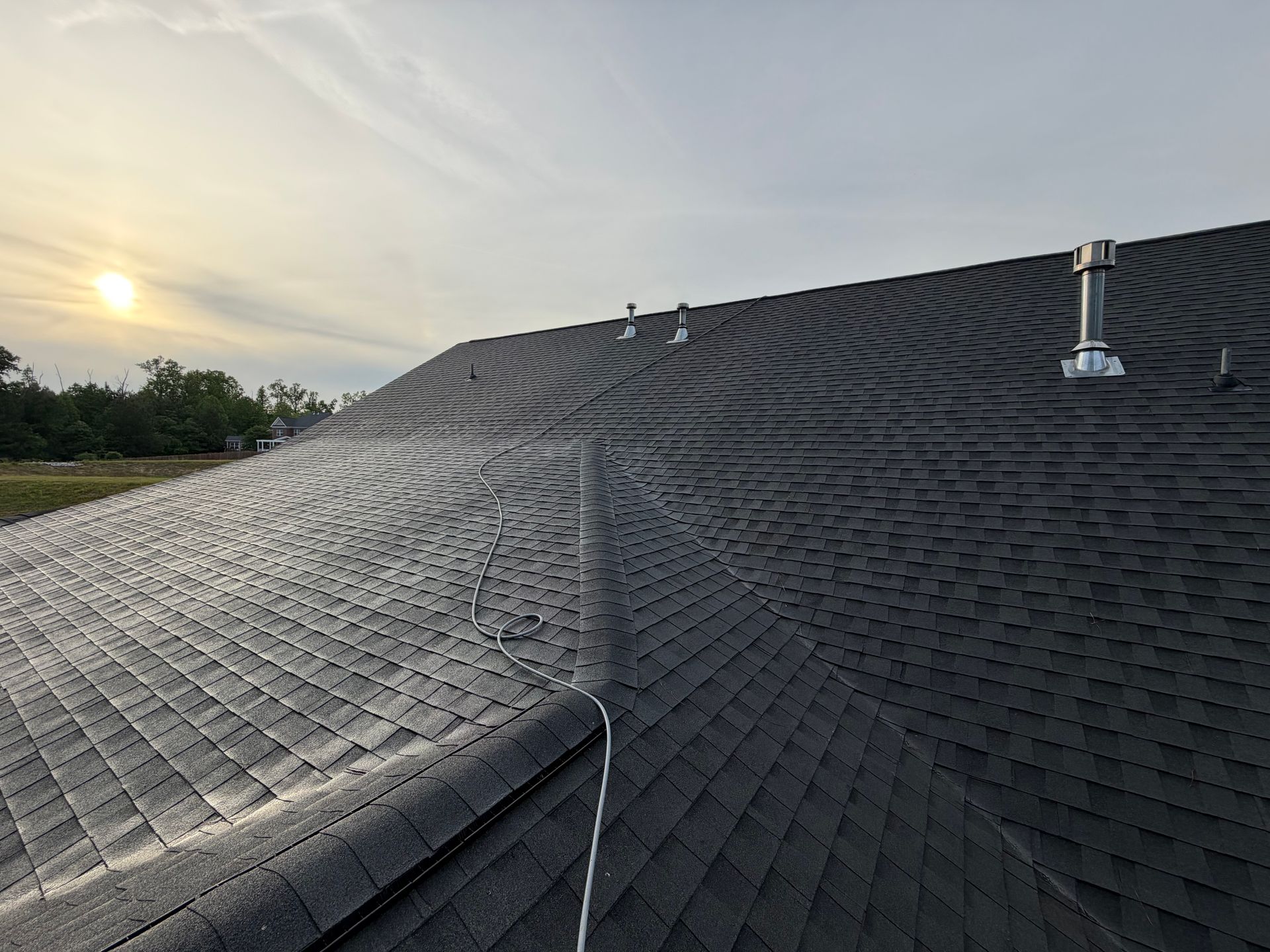 Dark shingled roof with skylight vents at sunset, viewed from the rooftop edge