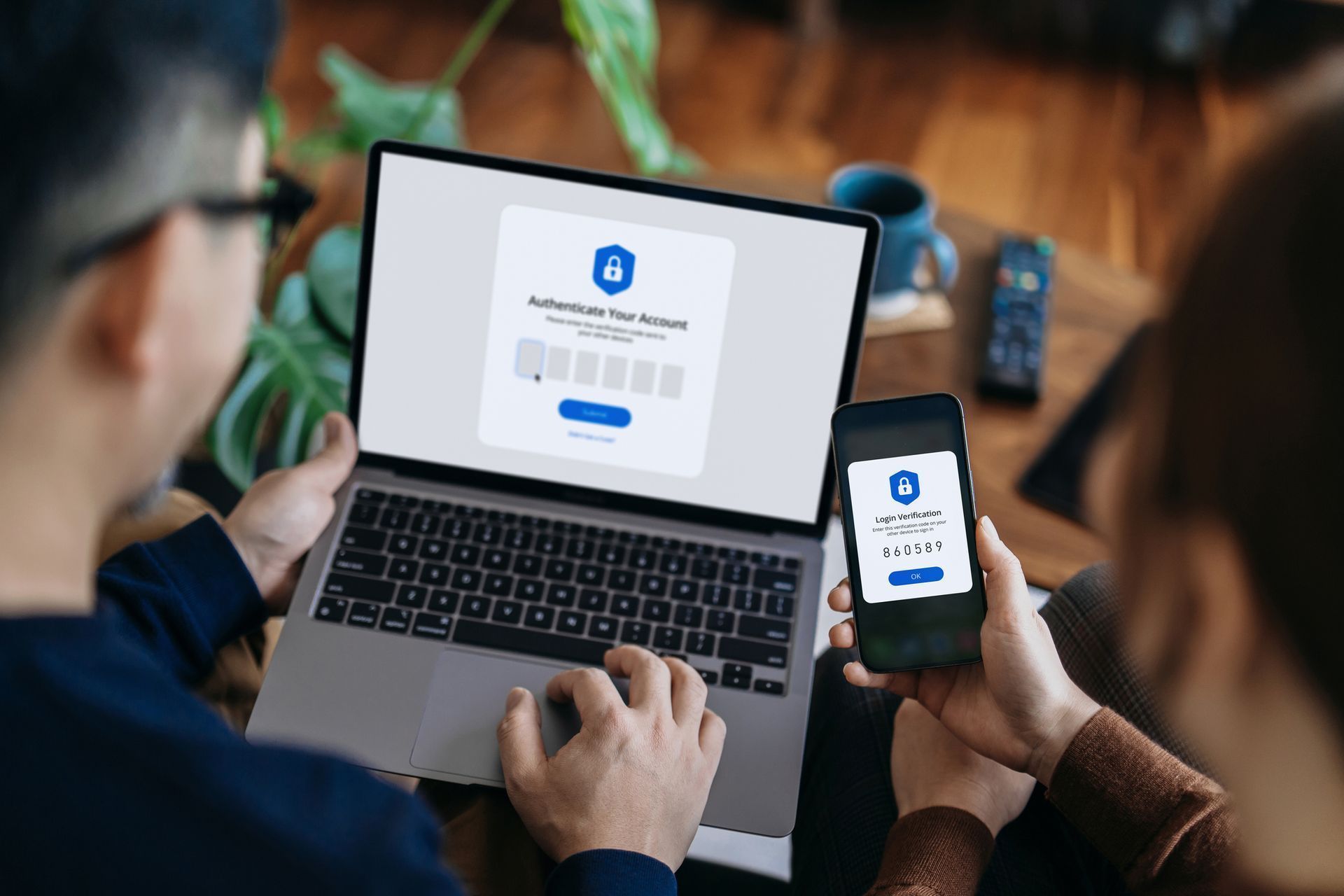 A man is using a laptop and a woman is holding a cell phone.