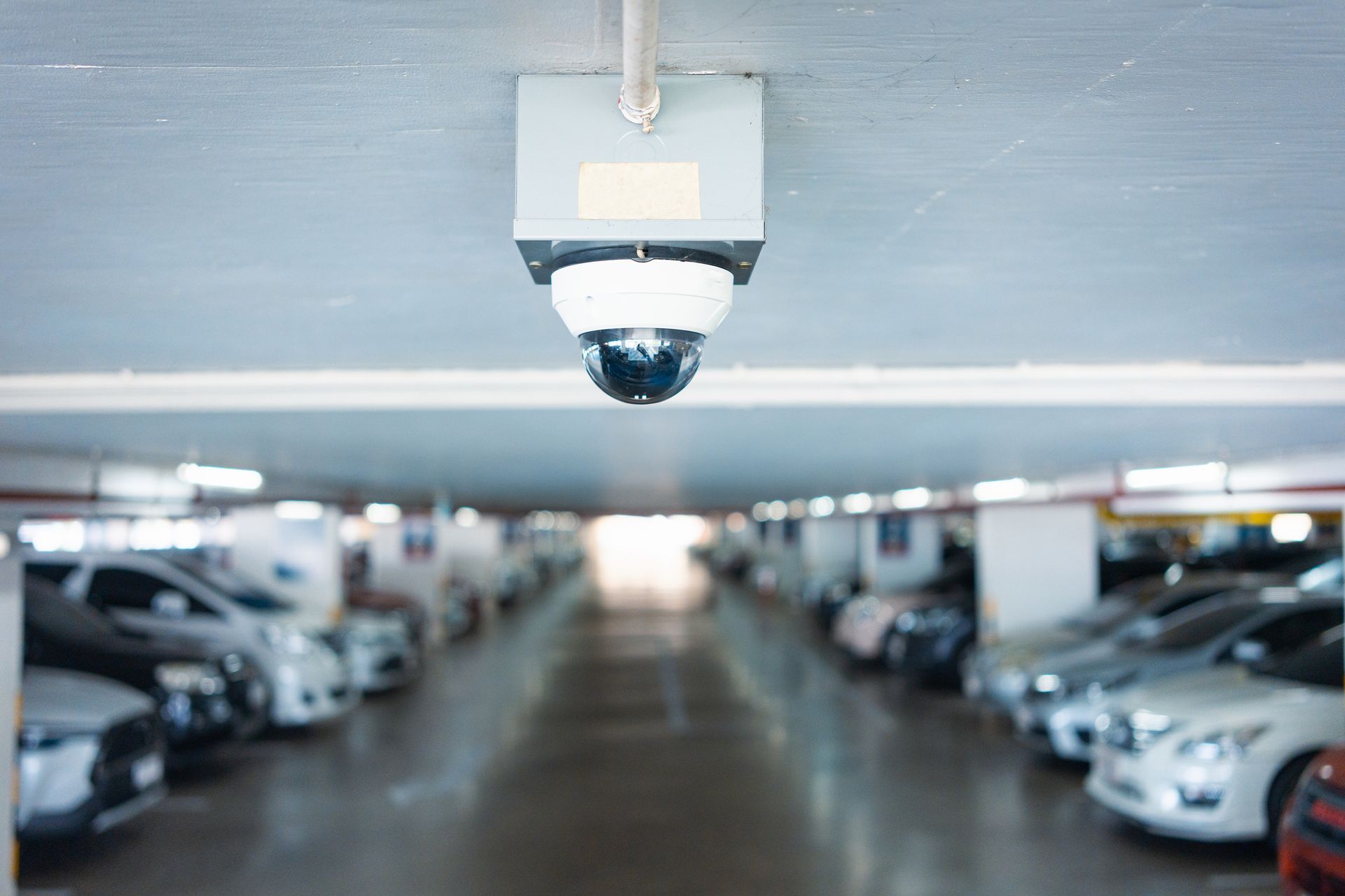 A security camera is hanging from the ceiling of a parking garage.