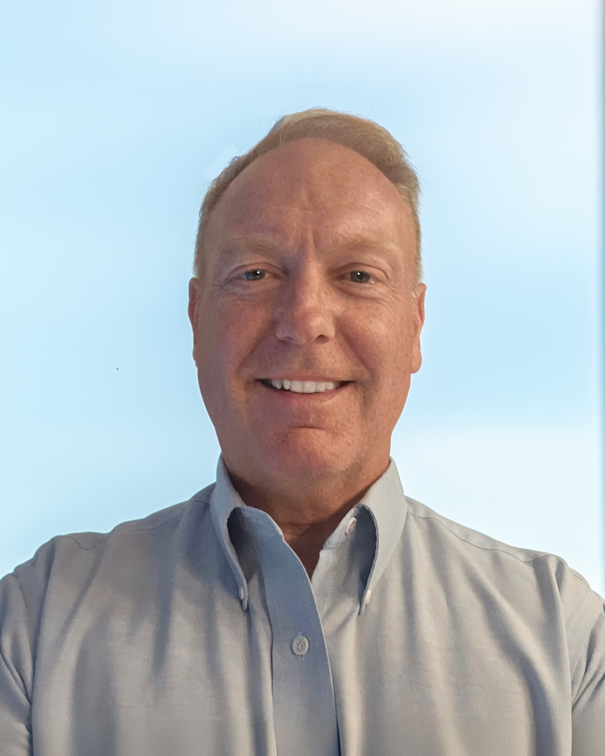 A man in a grey shirt and tie is smiling for the camera.