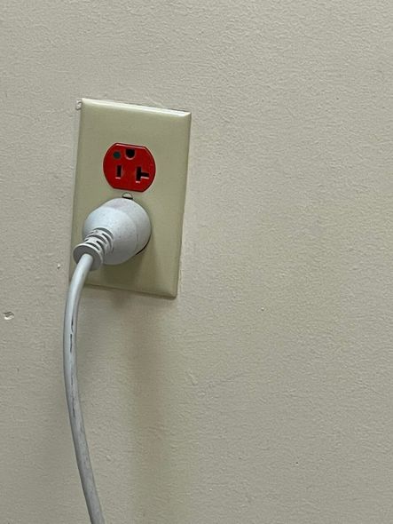 Red outlet with a white plug inserted into a beige wall.