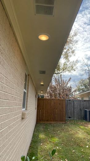 Beige brick house exterior with soffit lights and a wooden fence in the background.