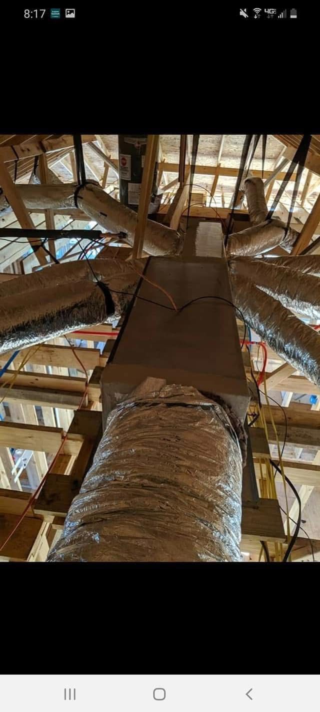 View inside an attic showing ductwork and a central air unit, supported by wooden beams.