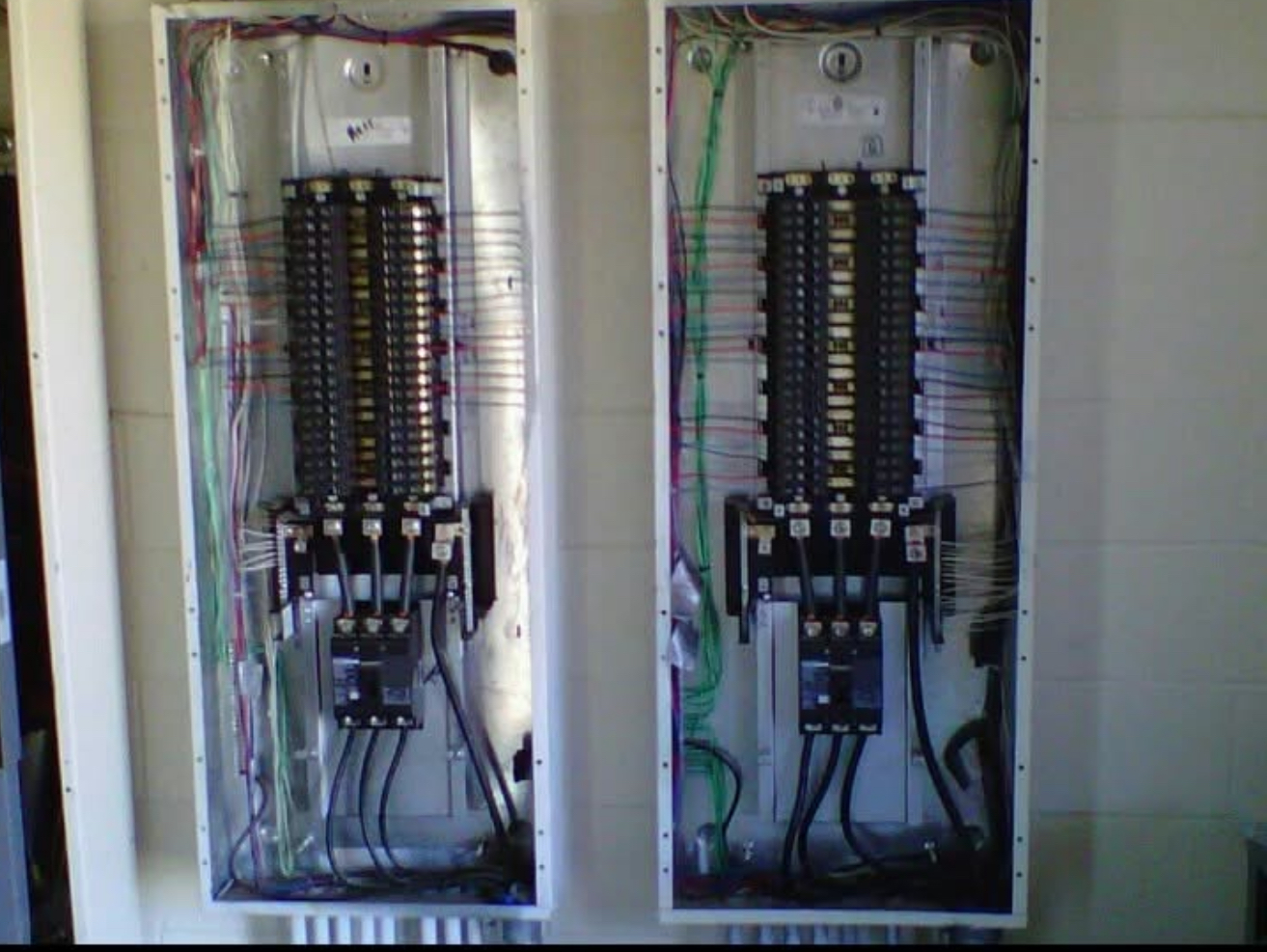 Two open, gray electrical breaker panels with numerous wires and black breakers.