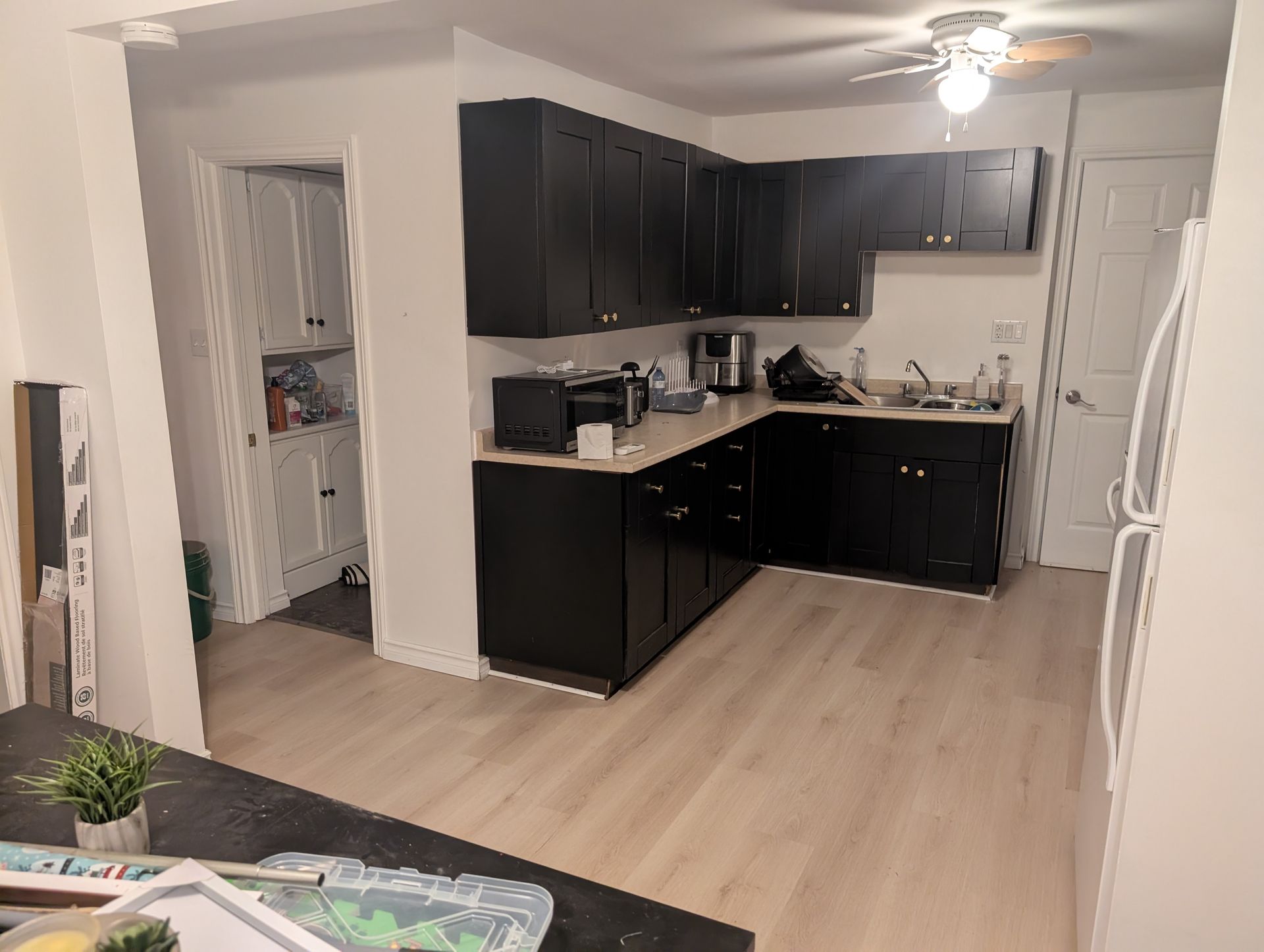 Man sanding wood in a workshop, wearing an apron and plaid shirt. Sunlight streams in.