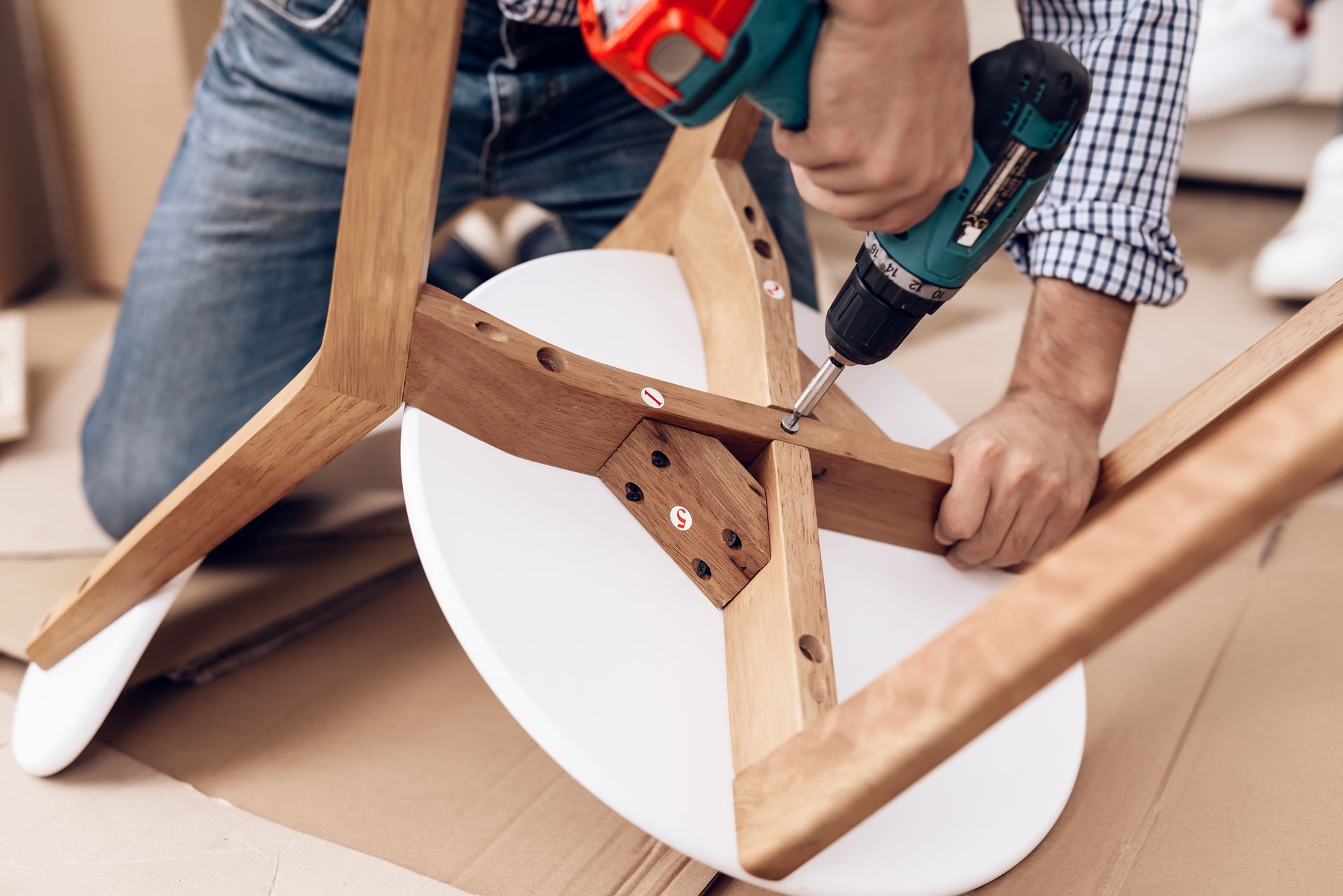 Person assembling a wooden chair with a power drill.