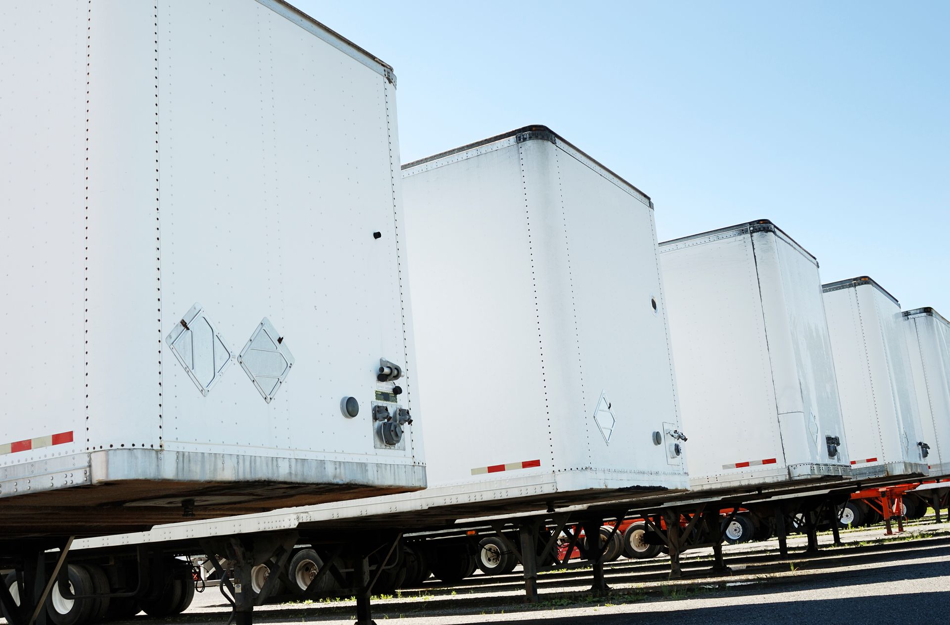 Row of white semi-truck trailers on a clear blue sky, showcasing reliable trailer rentals.
