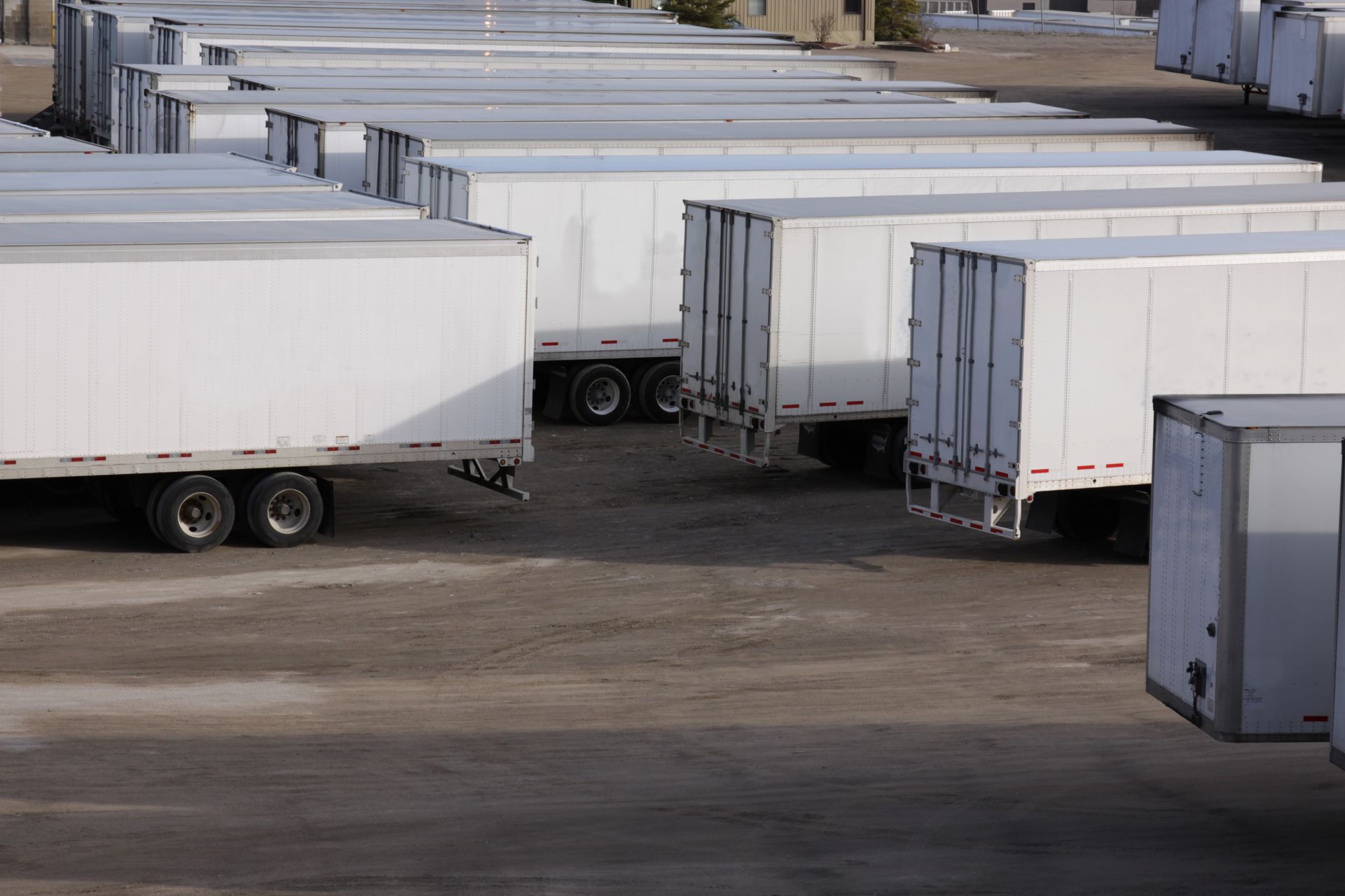 Rows of white semi-trailers parked in a dirt lot.