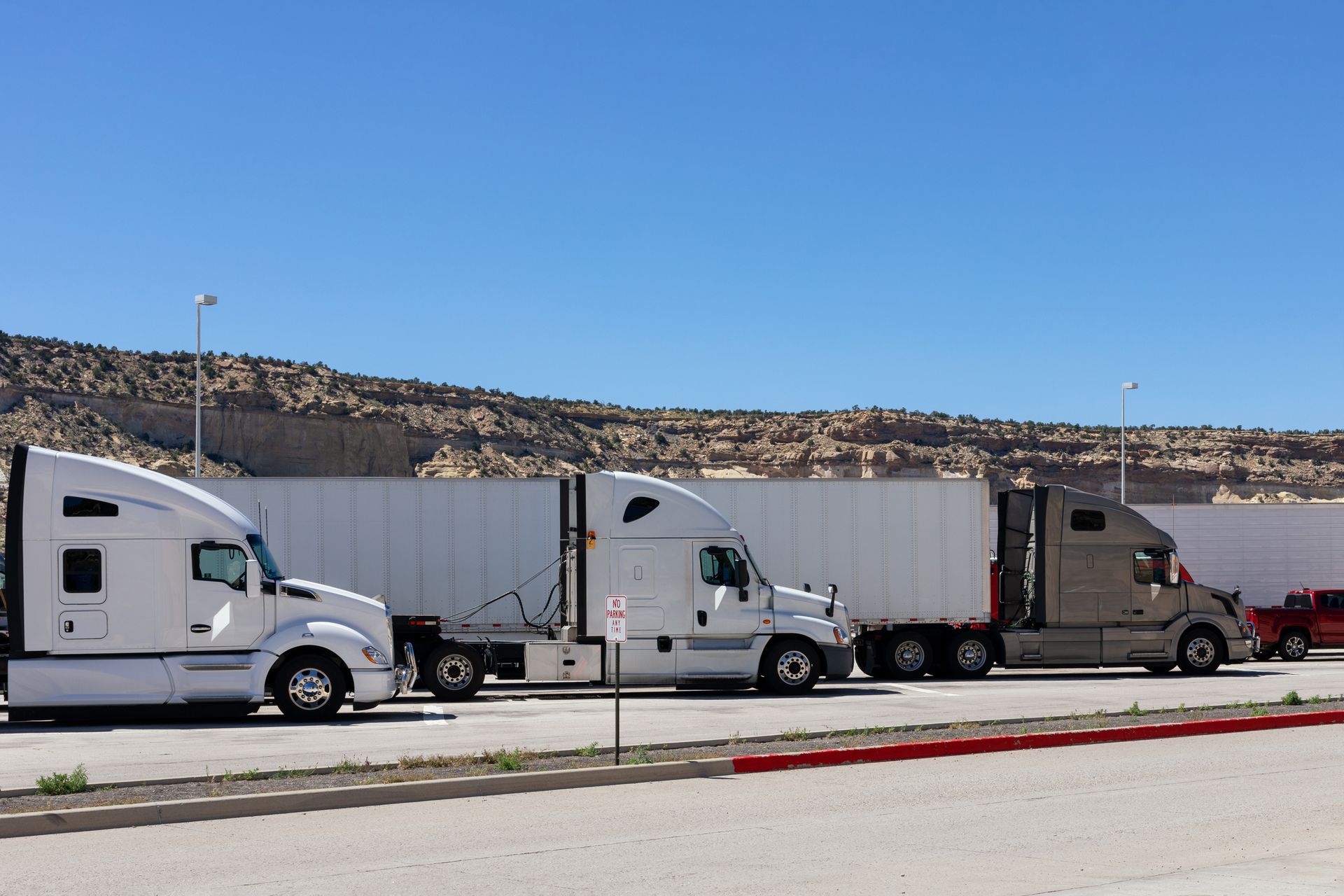 Three semi-trucks parked side by side in a rocky desert lot.