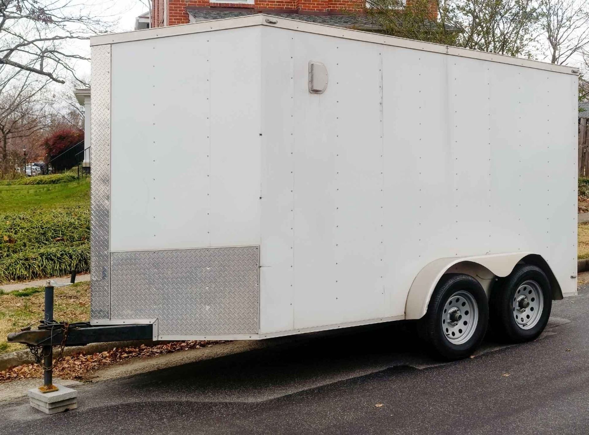 Front view of a small white cargo trailer parked on a neighborhood street