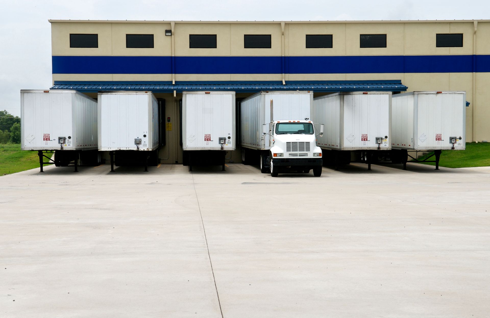 Six trailers at beige loading dock with grassy areas on both sides.