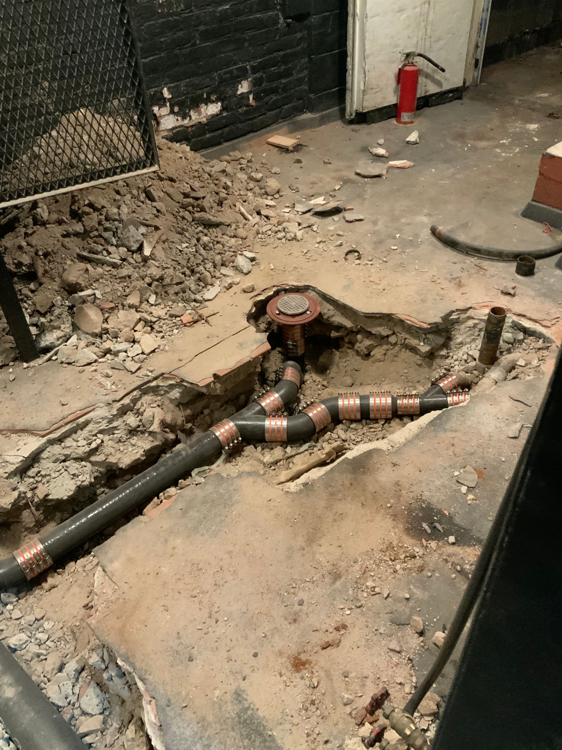 A fire extinguisher is sitting on the floor next to a hole in the ground.