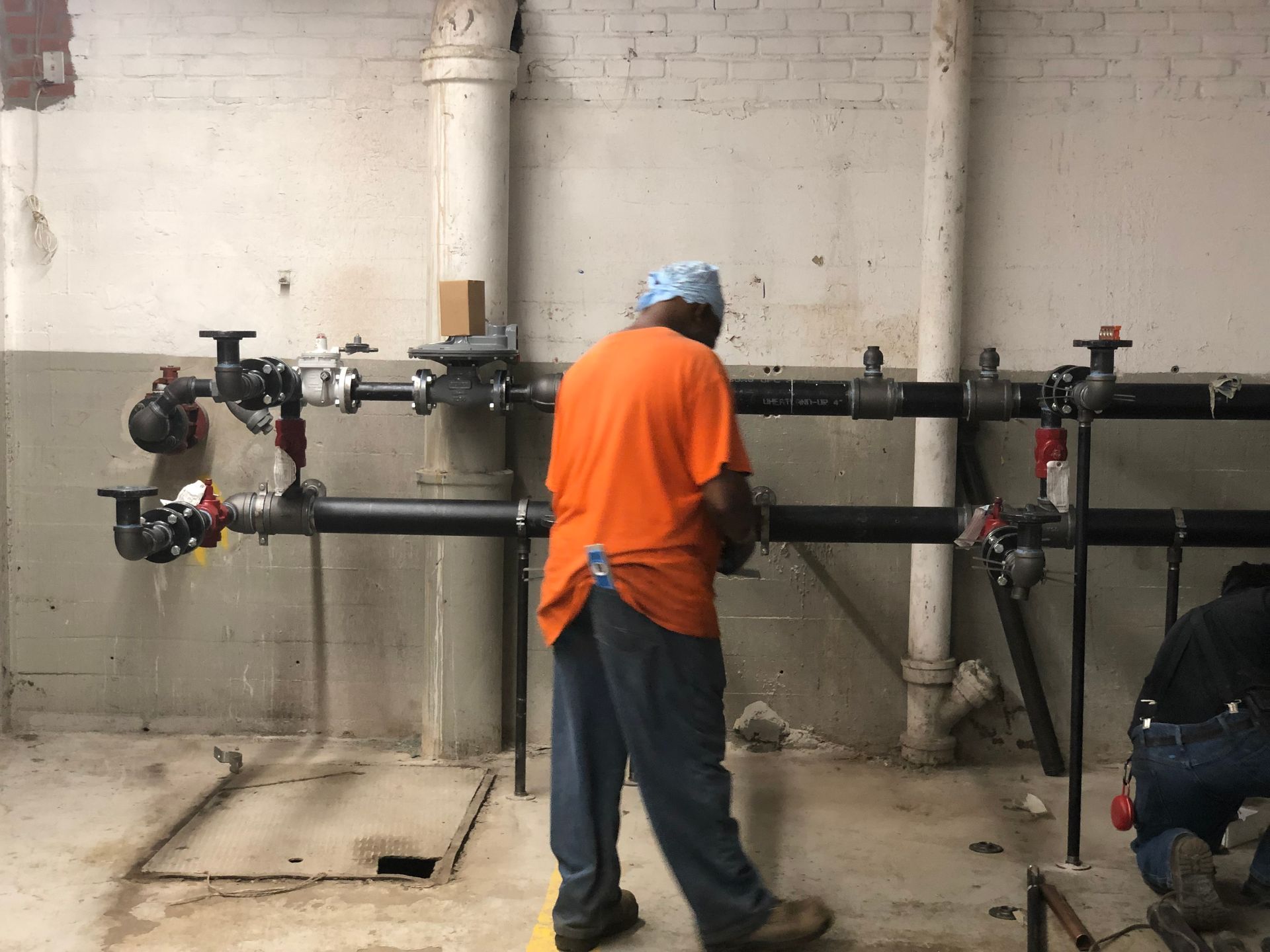 A man in an orange shirt is working on pipes in a room