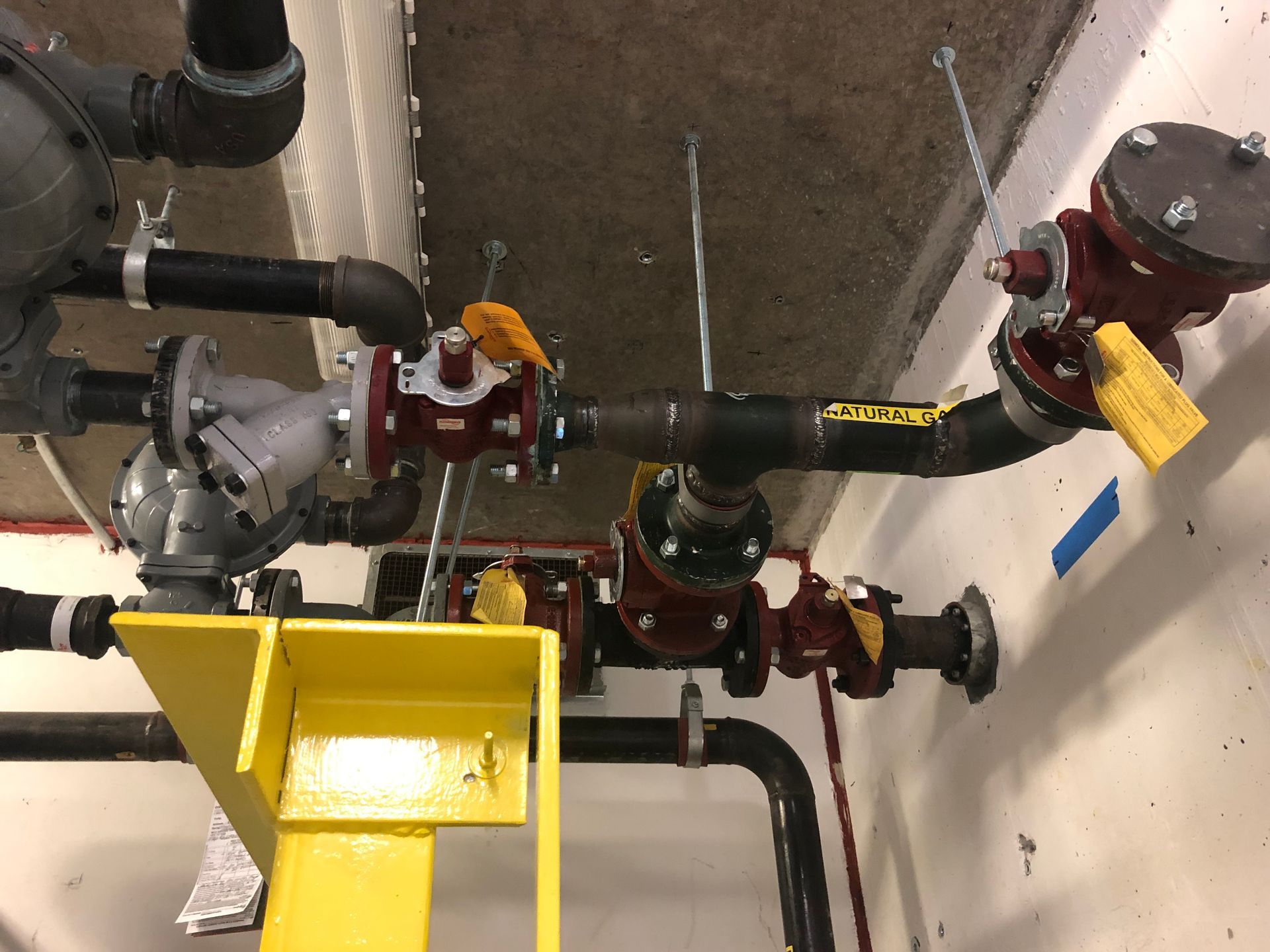A bunch of pipes and valves in a room with a yellow tag that says ' safety ' on it