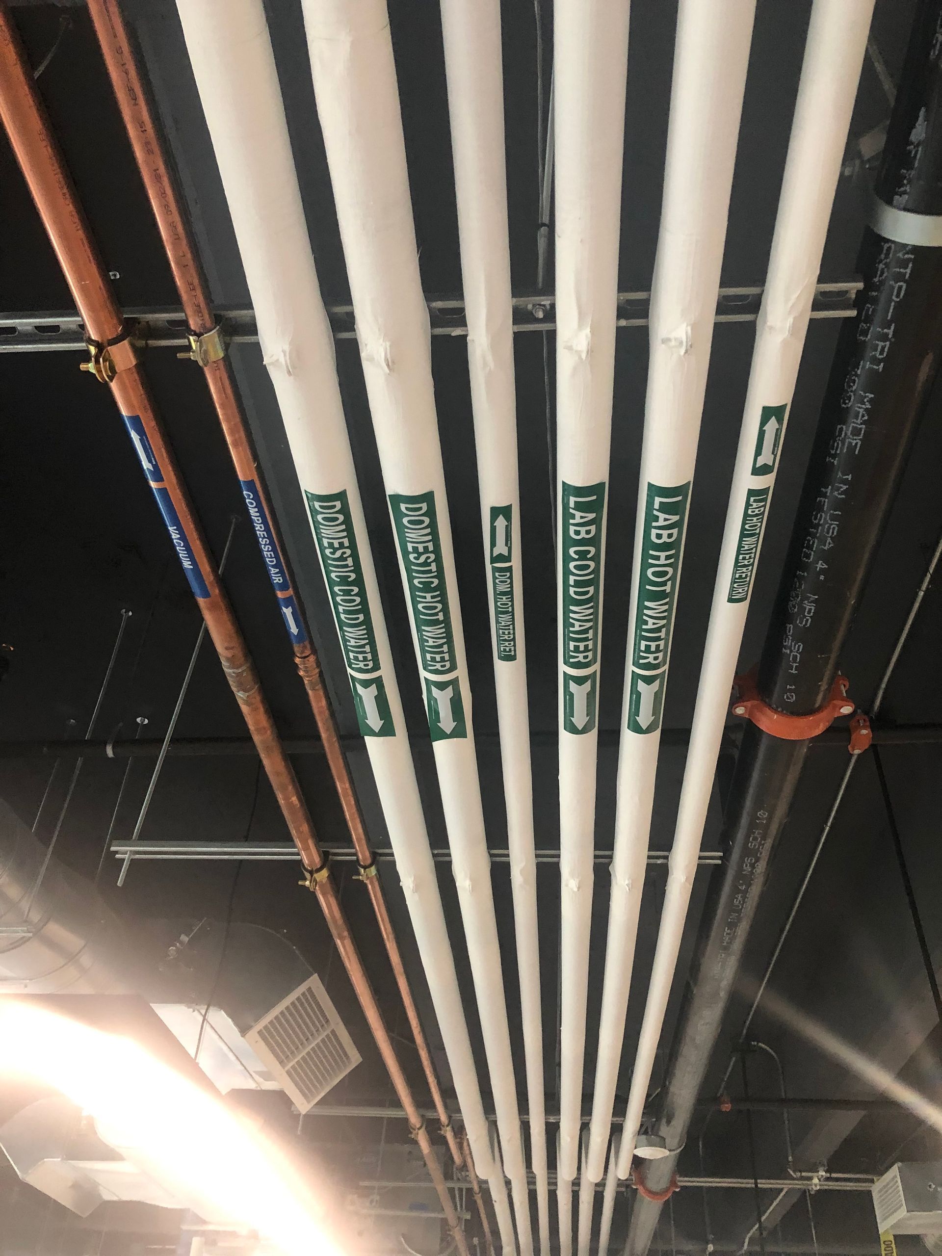 A row of pipes hanging from the ceiling with one that says ' ice cold water ' on it