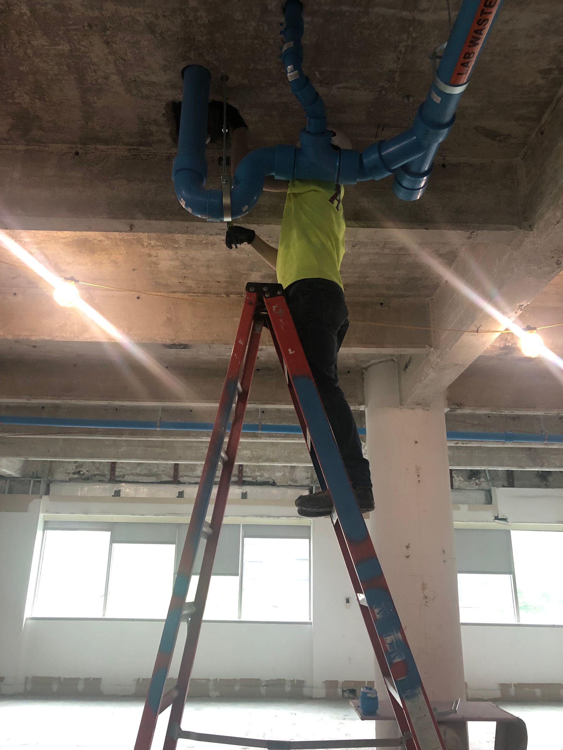 A man is standing on a ladder fixing pipes on the ceiling.